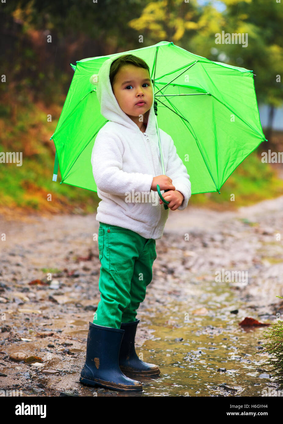 Baby Girl avec un parapluie sous la pluie coule dans les flaques en jouant sur la nature Banque D'Images