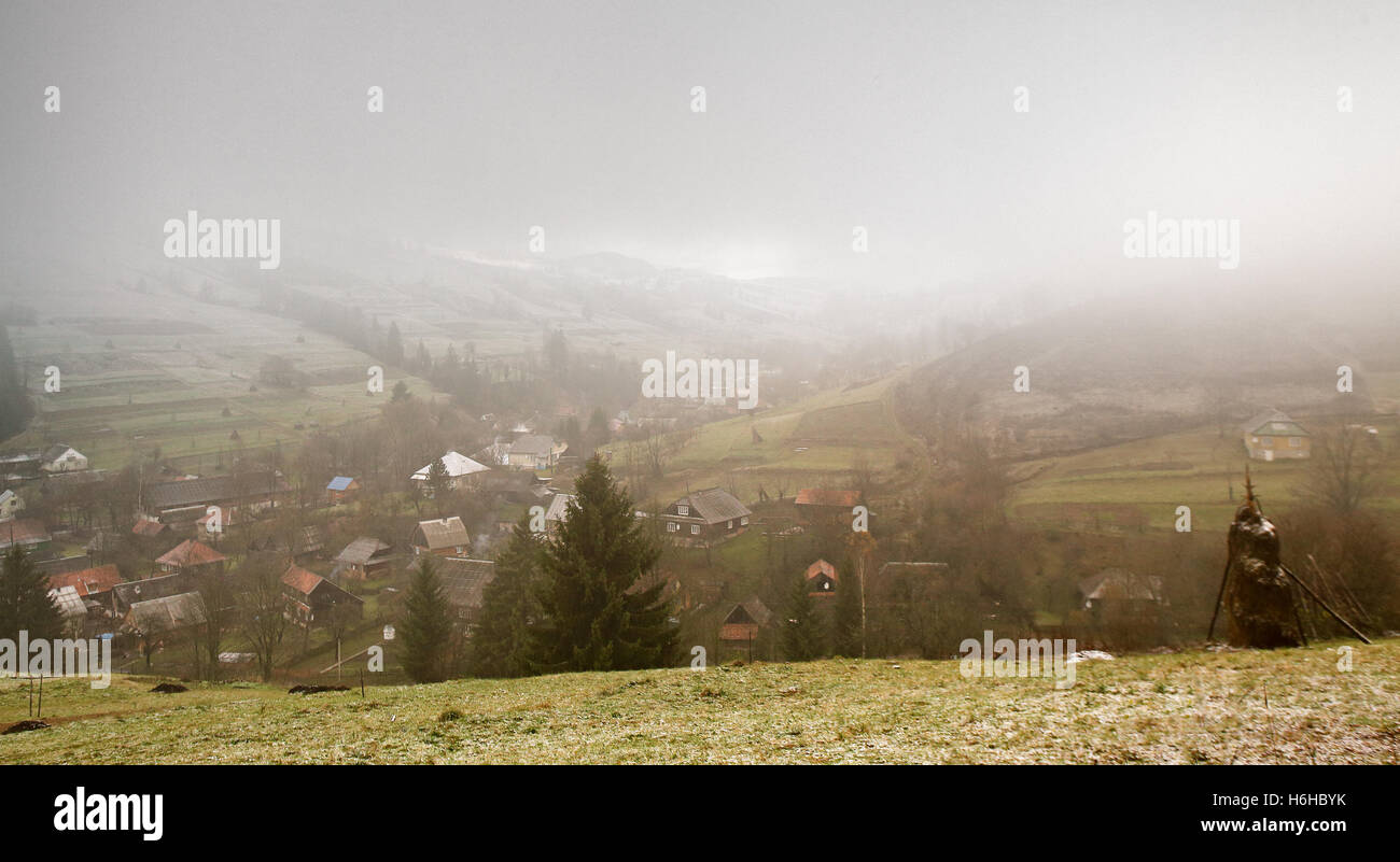 La fin de l'automne matin brumeux dans un village. Première neige en montagne Banque D'Images