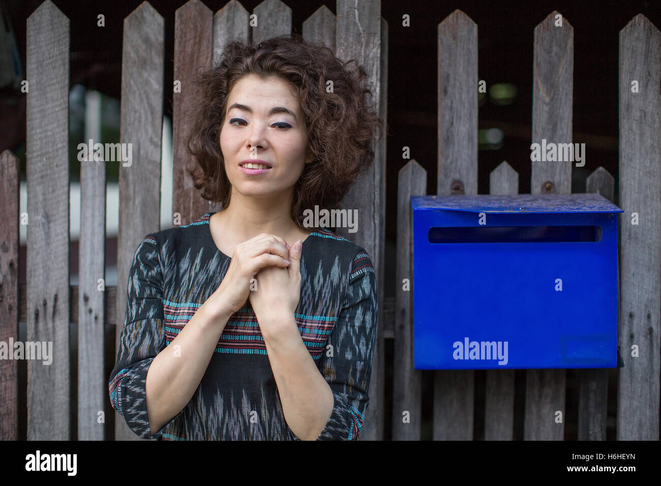 Young Asian woman standing dans la rue près de la clôture en bois avec une boîte aux lettres. Banque D'Images