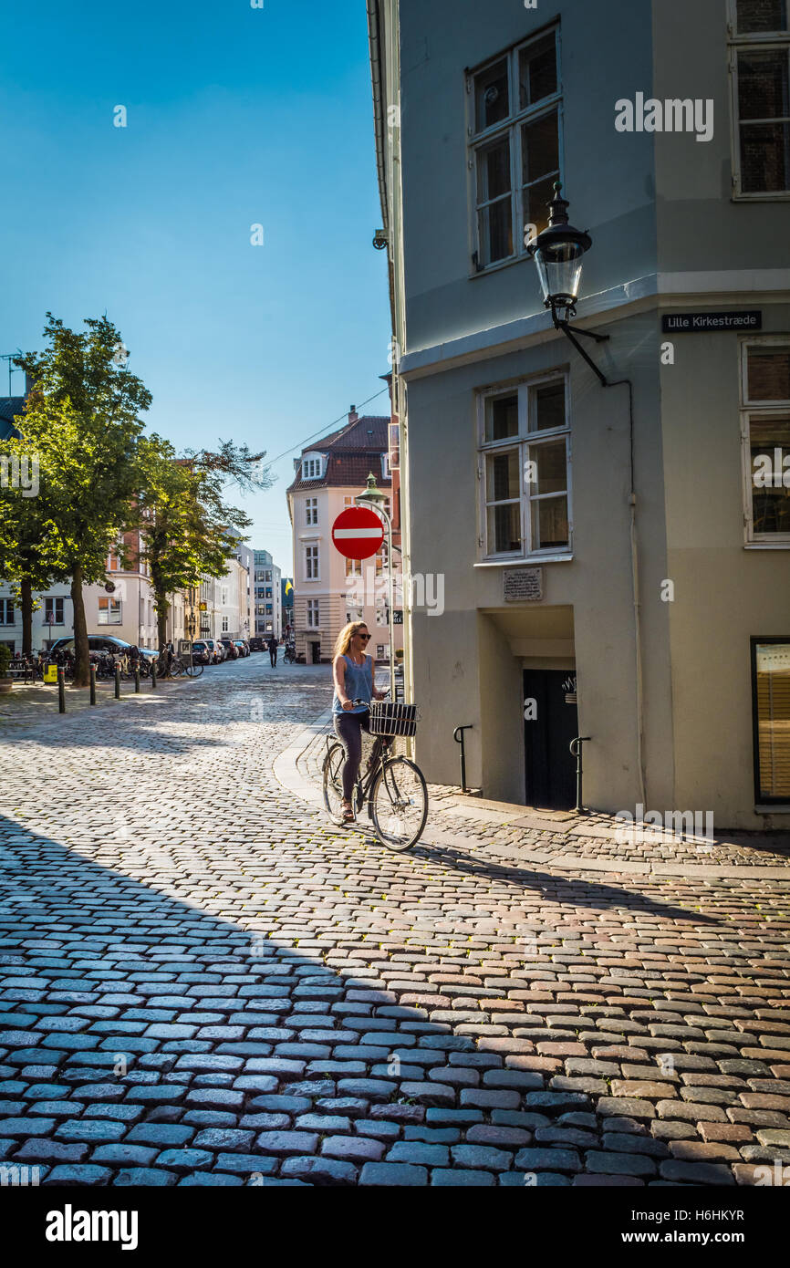 Une jeune femme sur un vélo dans une rue pavée, à Copenhague, au Danemark, de l'Union européenne. Banque D'Images