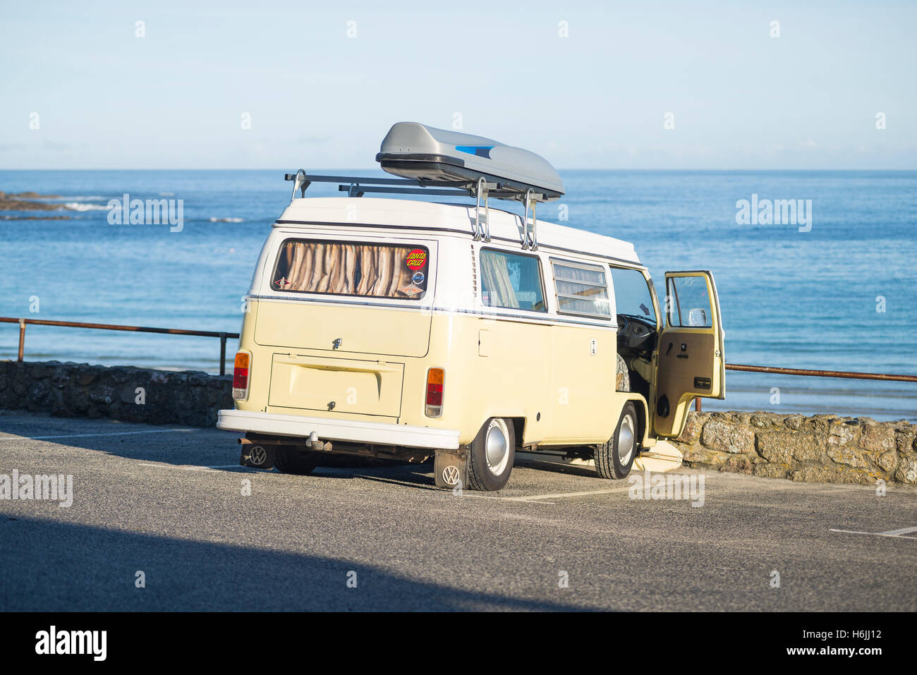 Une Volkswagen Bulli bus vintage camping à Sennen Cove parking plage donnant sur la mer bleue dans le soleil du matin en été, Cornwall, UK Banque D'Images
