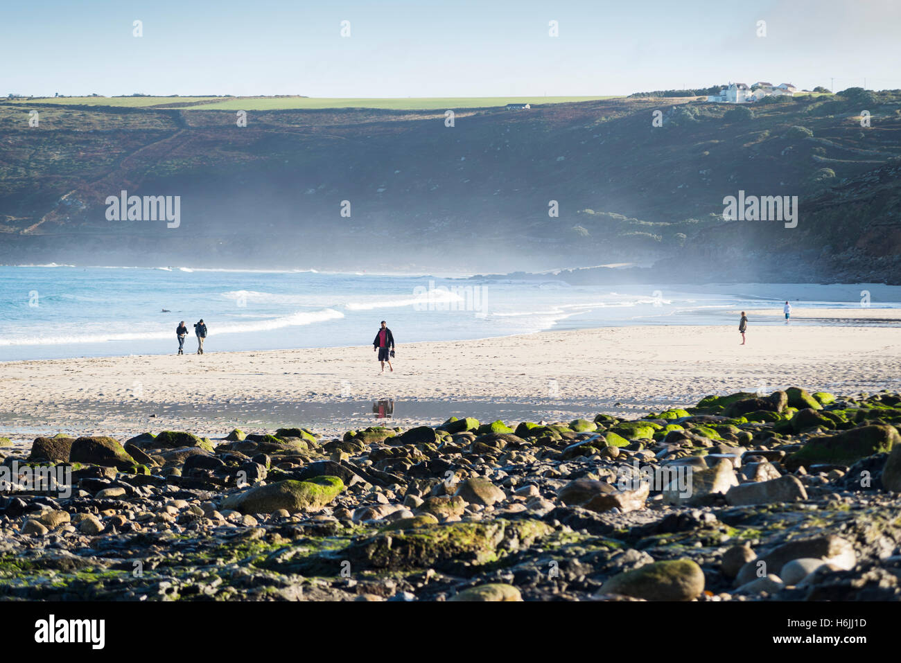Les gens qui marchent sur la plage de sable dans le jet de l'océan Atlantique surf à marée basse après le lever du soleil à Sennen Cove, sur la côte ouest de Cornwall, UK Banque D'Images