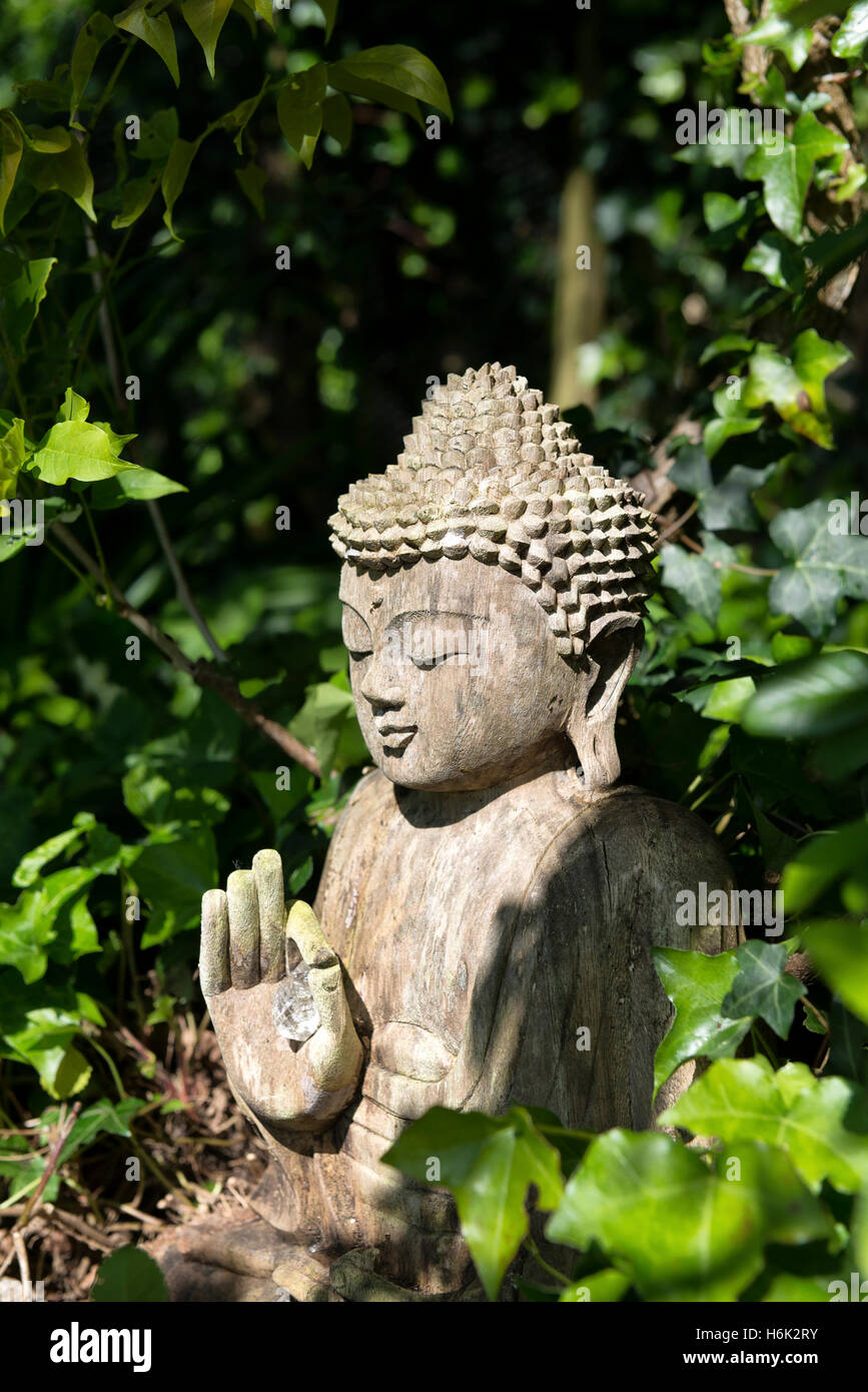 Buddah tenant une pierre crystal se trouve sereinement dans un pays ensoleillé jardin entouré de feuilles de lierre devon Banque D'Images