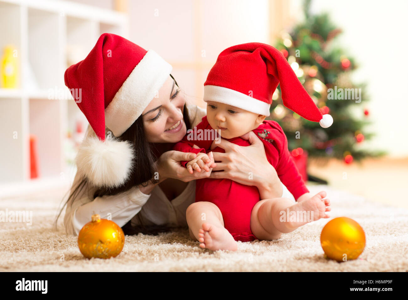 La mère et l'enfant en robe rouge santa sourire sur un fond d'arbres de Noël dans l'intérieur de la chambre Banque D'Images