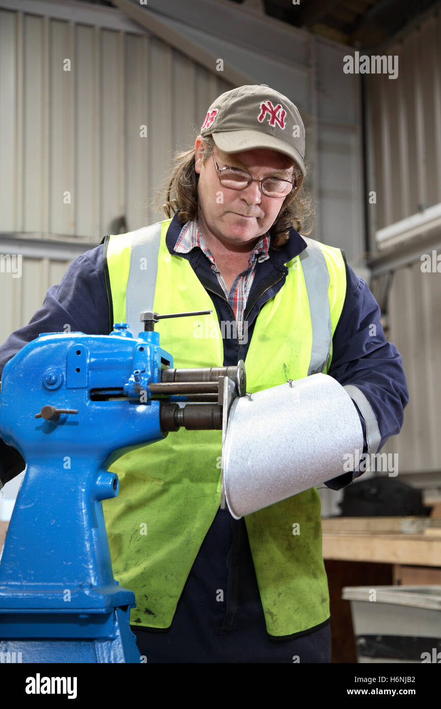 Un travailleur roule une bande métallique dans un atelier de fabrication sur mesure des sections du conduit d'air pour manipulant des Banque D'Images