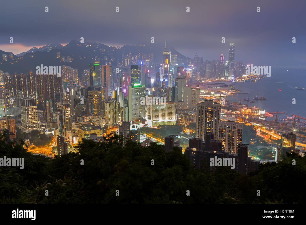 Gratte-ciel allumé sur l'île de Hong Kong à Hong Kong, Chine, vu de la Braemar Hill sur un brumeux et nuageux le soir. Banque D'Images