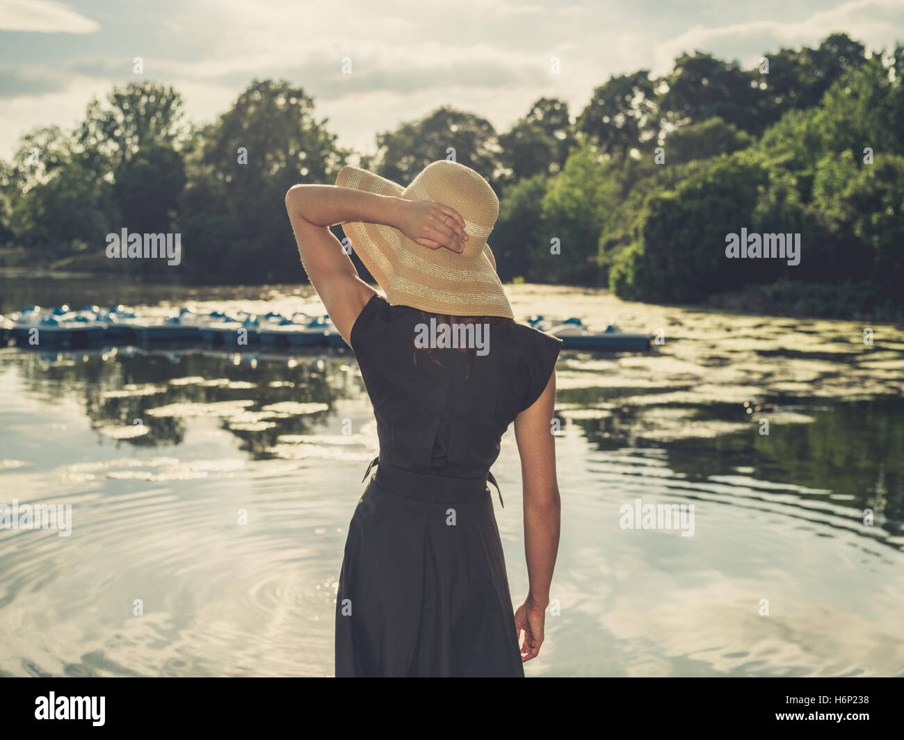 Vintage photo de filtré une femme élégante portant un chapeau debout au bord d'un lac dans un parc au coucher du soleil Banque D'Images