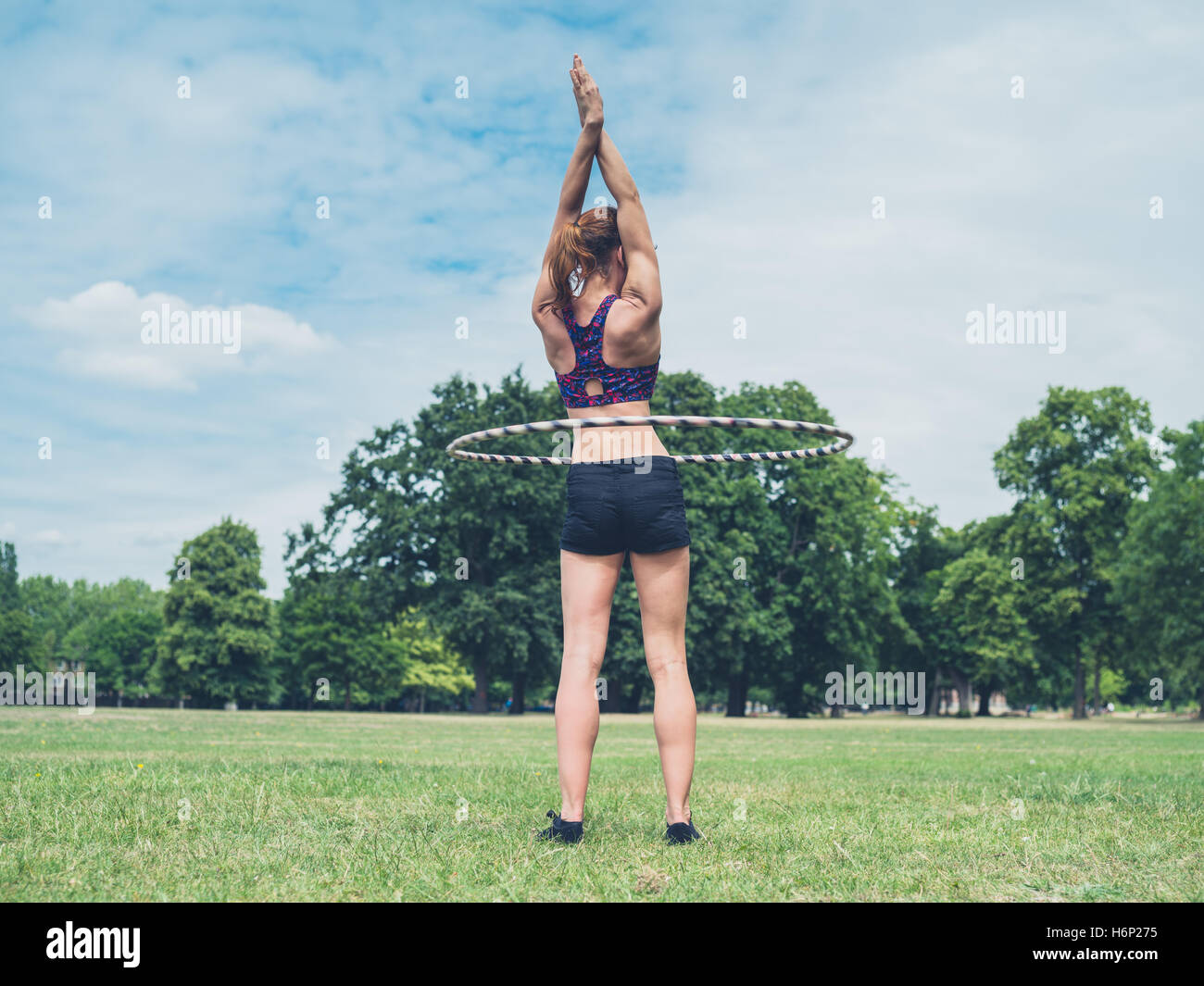 Un ajustement et athlétique jeune femme travaille avec un cerceau dans le parc sur une journée ensoleillée Banque D'Images