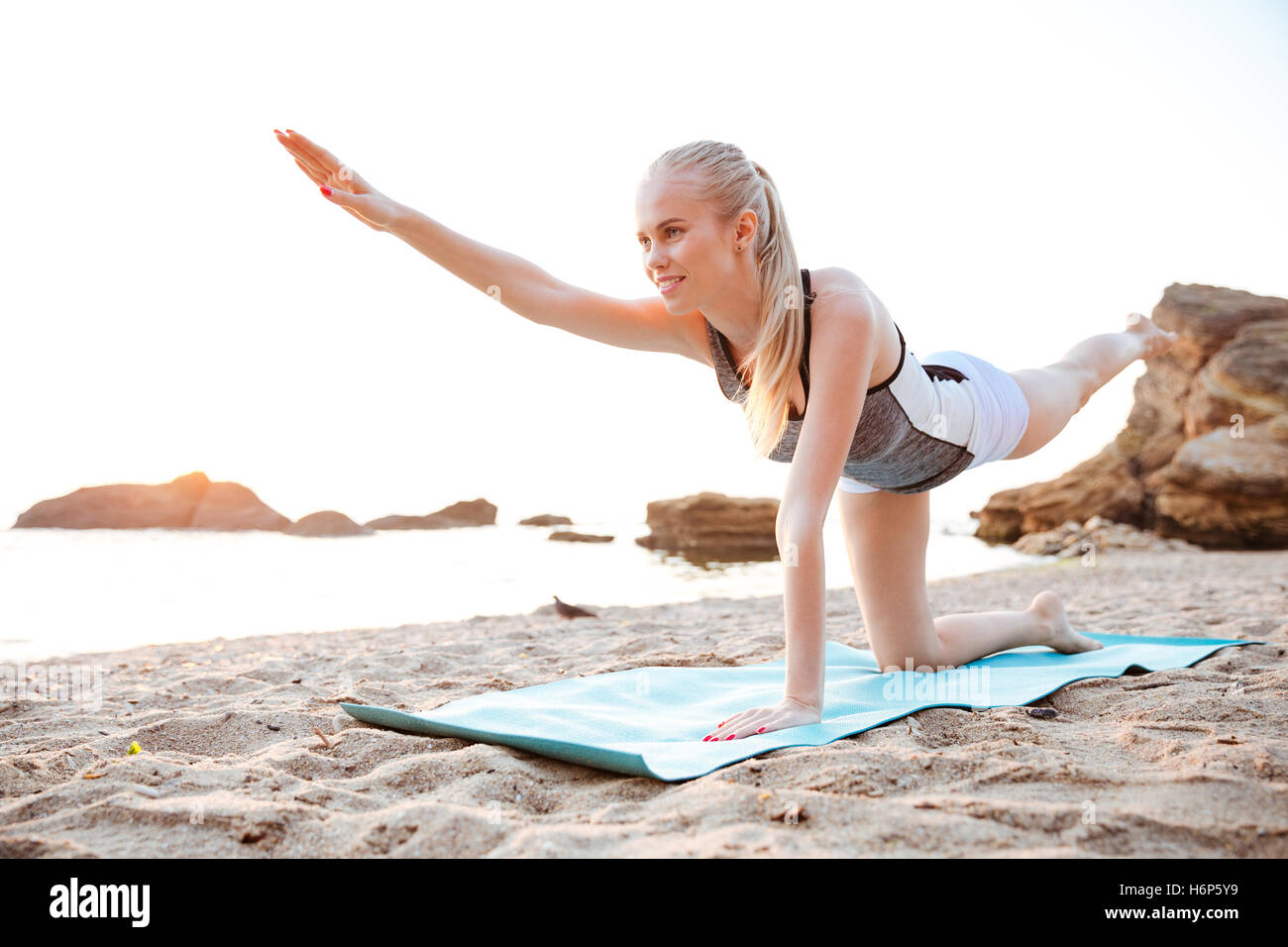 Portrait d'une charmante femme stretching on yoga mat sur la plage le matin Banque D'Images