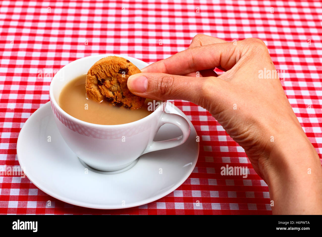 Femme-chers-filles part tremper un biscuit cookie dans d'une tasse de thé chaud avec une croix rouge et blanc tissu table vérifiées Banque D'Images