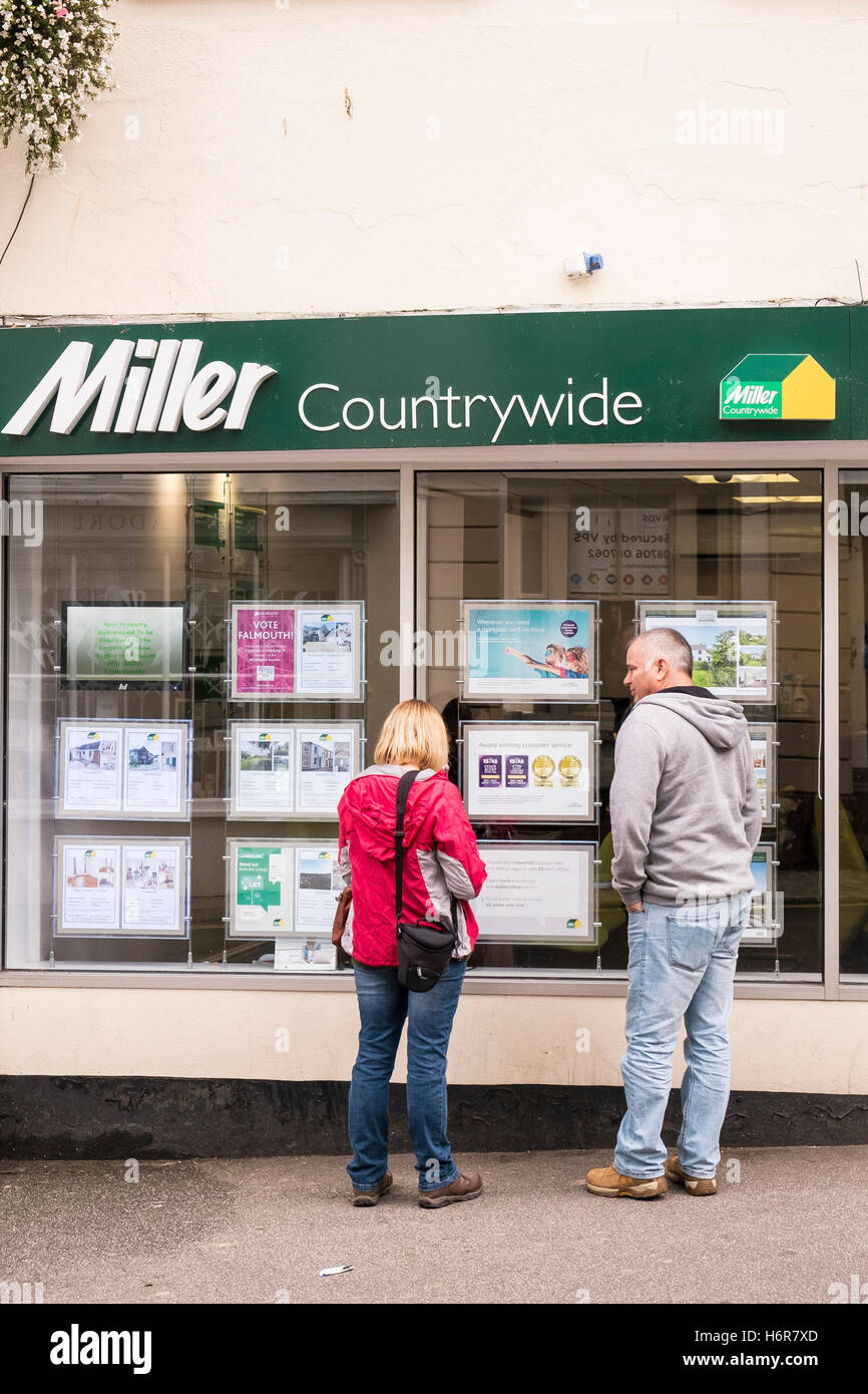 Deux personnes à la recherche à l'intérieur de la propriété dans une fenêtre d'agents immobiliers à Falmouth, Cornwall. Banque D'Images