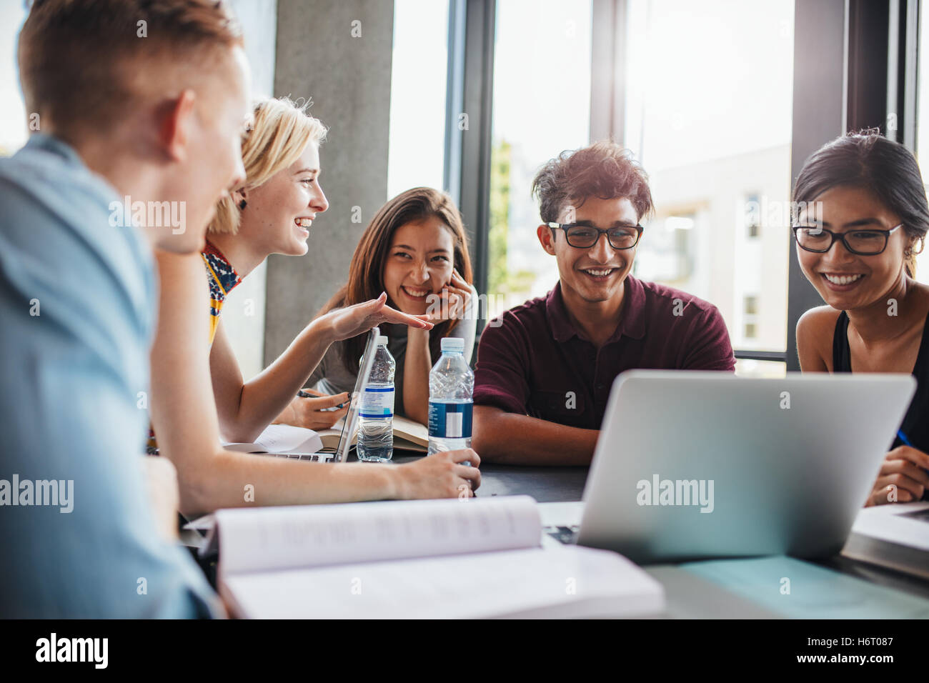 étudiants universitaires assis ensemble à table avec des livres et un ordinateur portable. Jeunes heureux qui étudient en groupe à la bibliothèque. Banque D'Images