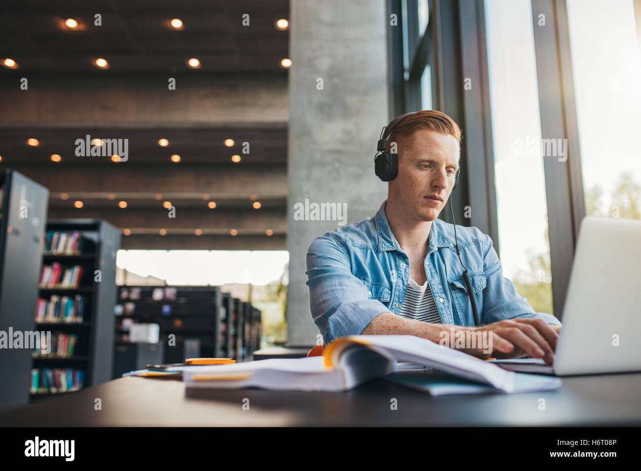 Jeune étudiant avec un casque d'étudier sur l'ordinateur portable. Handsome man assis au bureau et de travail sur l'ordinateur portable à p Banque D'Images