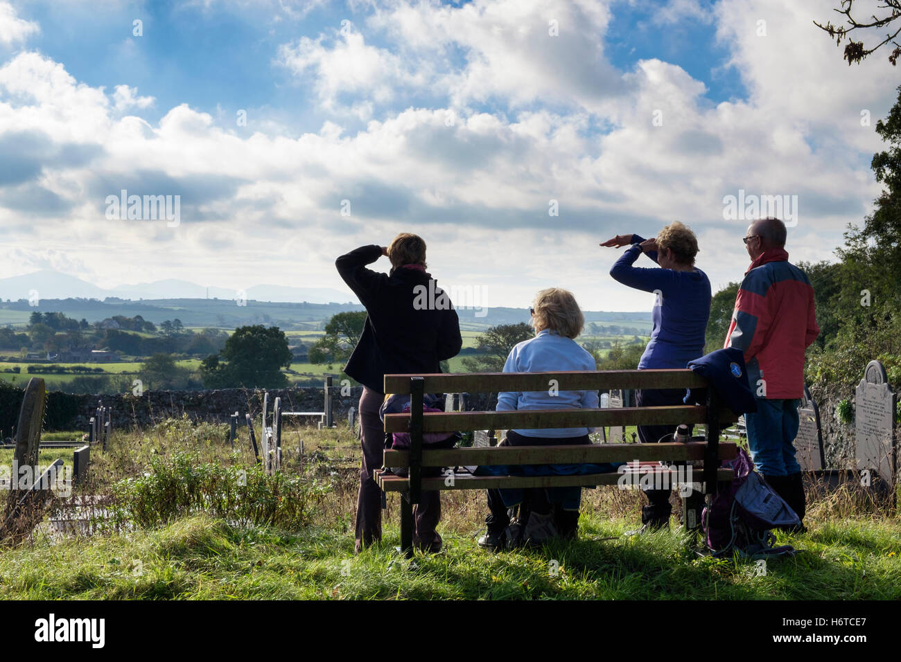 Les randonneurs se reposant sur un banc regardant vue depuis St Peter's churchyard de montagnes au loin. Llanbedregoch Anglesey Pays de Galles UK Banque D'Images