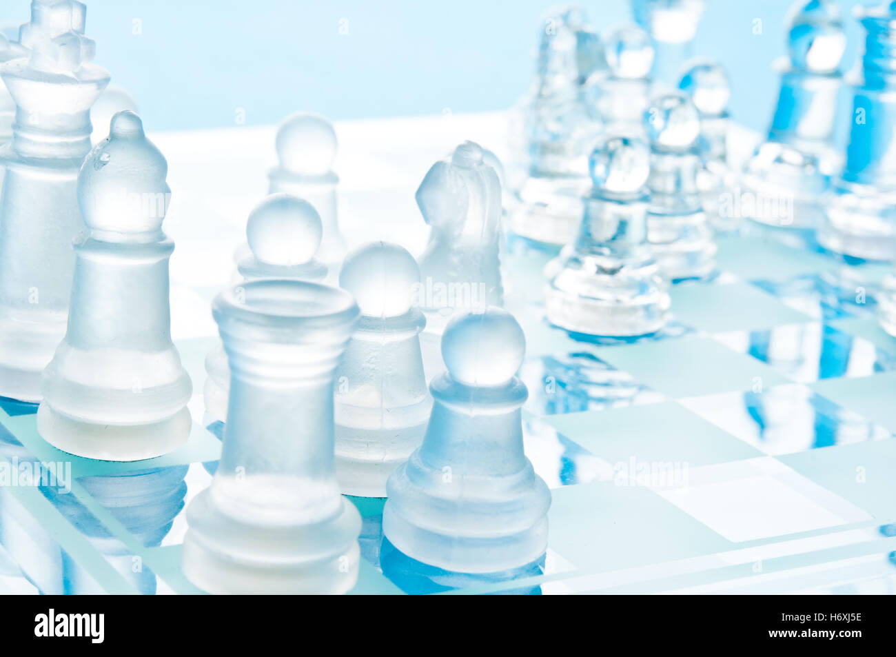 Des pièces d'échecs en verre clair et dépoli s'affrontent sur un échiquier en verre bleu dans une composition studio en gros plan lumineuse Banque D'Images