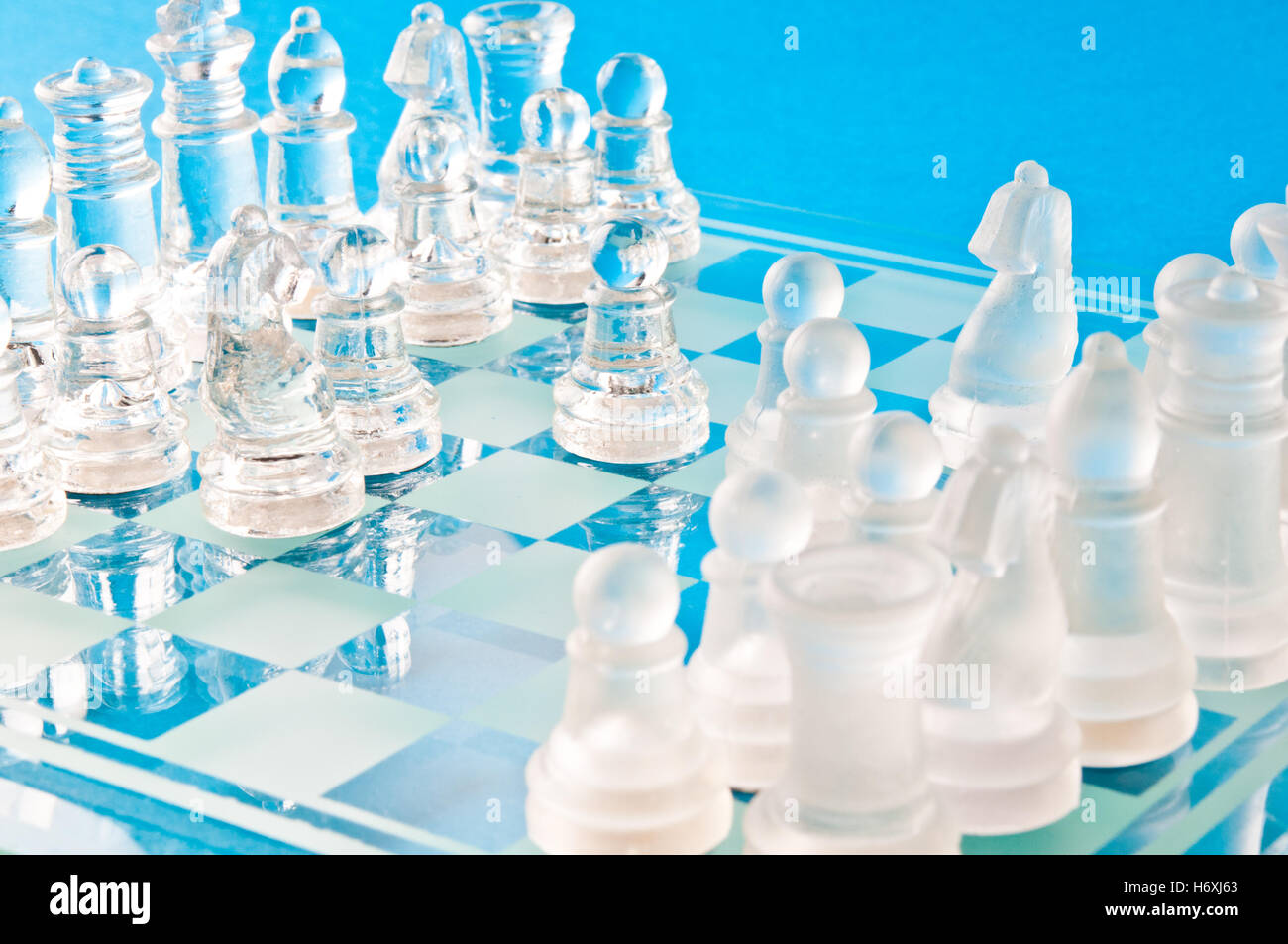 Des pièces d'échecs en verre clair et dépoli s'affrontent sur un échiquier en verre bleu dans une composition studio en gros plan lumineuse Banque D'Images
