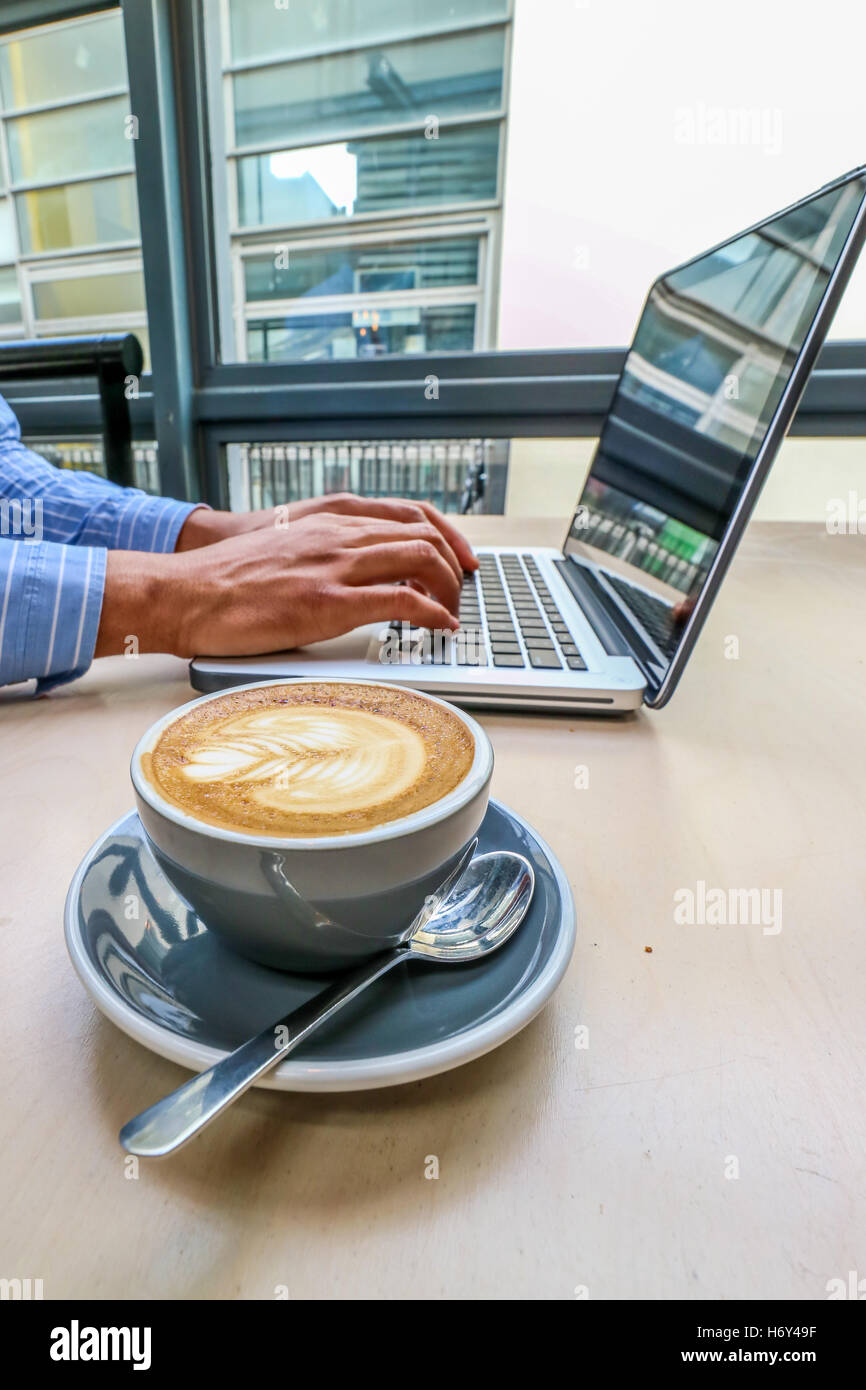 Un homme de race noire à l'aide d'un ordinateur portable avec du café Banque D'Images