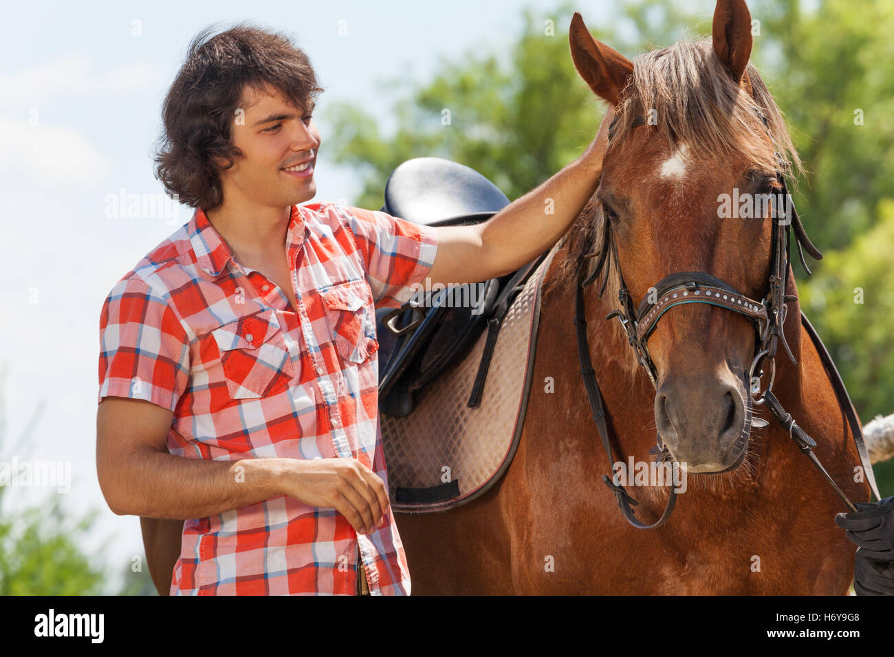 Heureux jeune homme caressant sa belle bay horse Banque D'Images