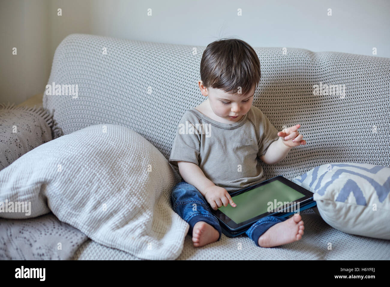 Baby Boy sitting on sofa using digital tablet touchscreen Banque D'Images