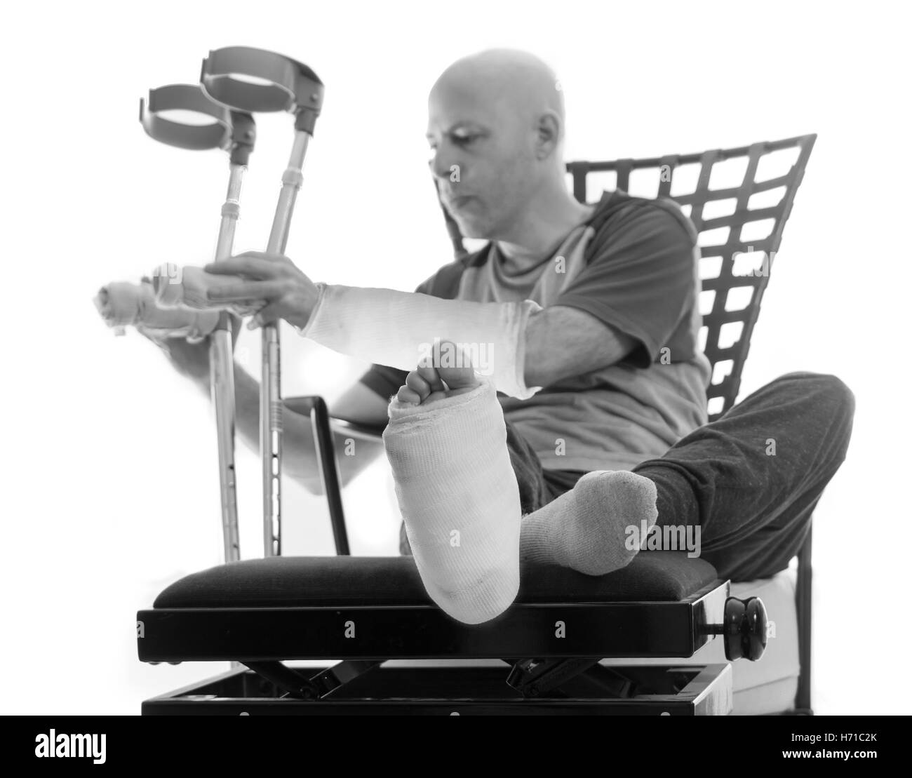 Jeune homme après un grave accident avec fracture de la cheville et du poignet et du plâtre et de plâtres en fibre de verre sur la jambe et le bras, mettant sa Banque D'Images