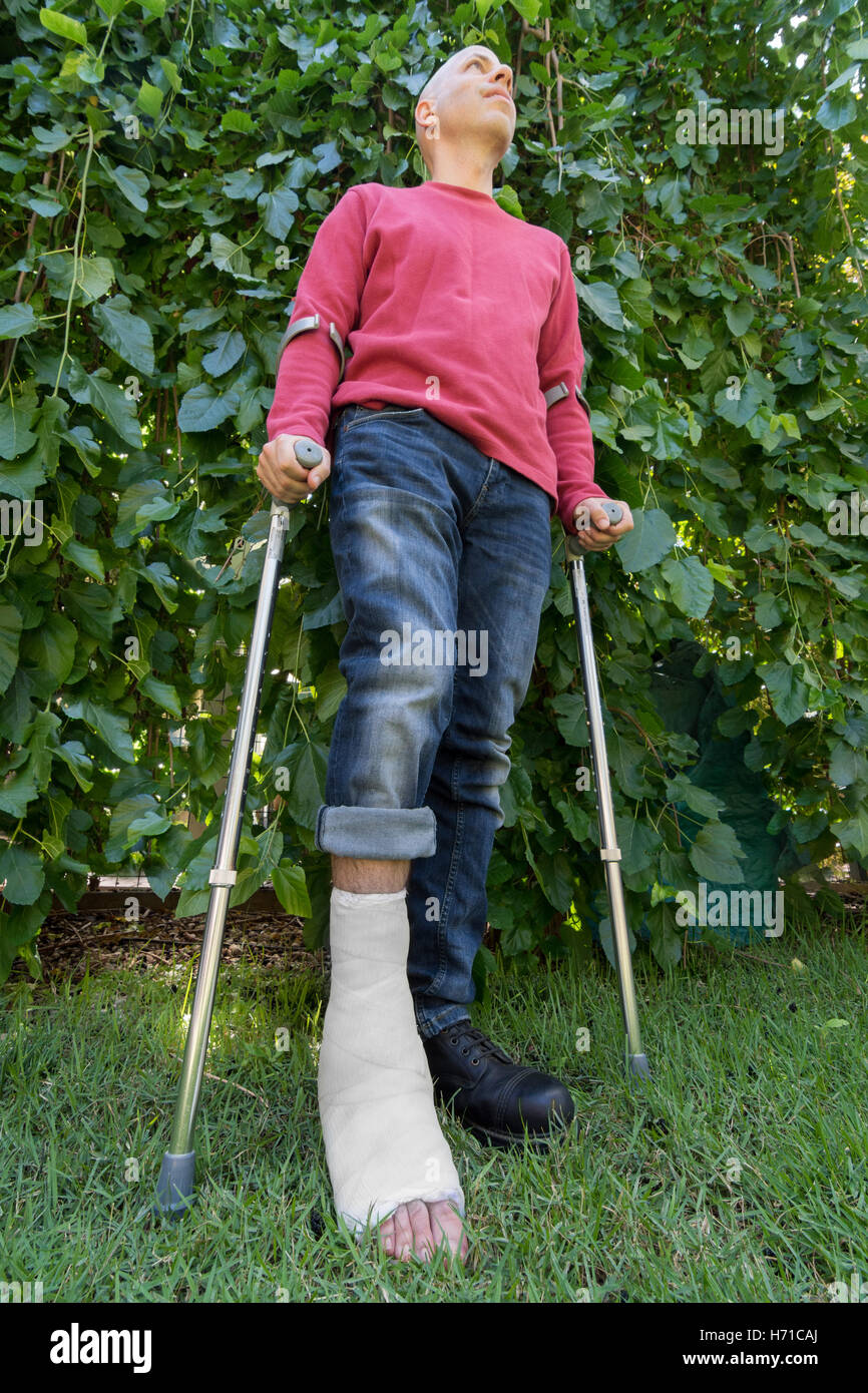 Jeune homme avec une cheville cassée et un plâtre en fibre de verre blanc et sur sa jambe, obtenir un peu d'air frais dans le jardin pendant que wal Banque D'Images