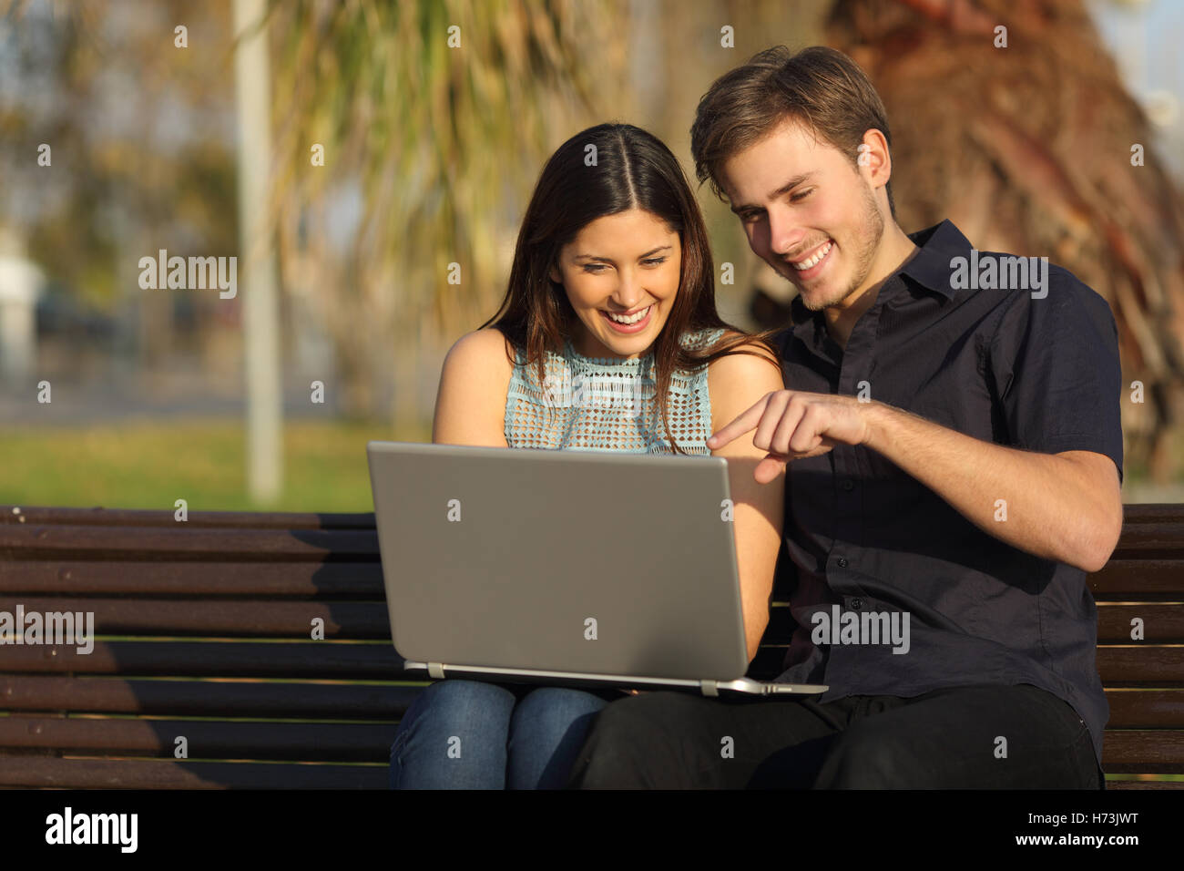 Couple watching médias dans un ordinateur portable assis sur un banc Banque D'Images