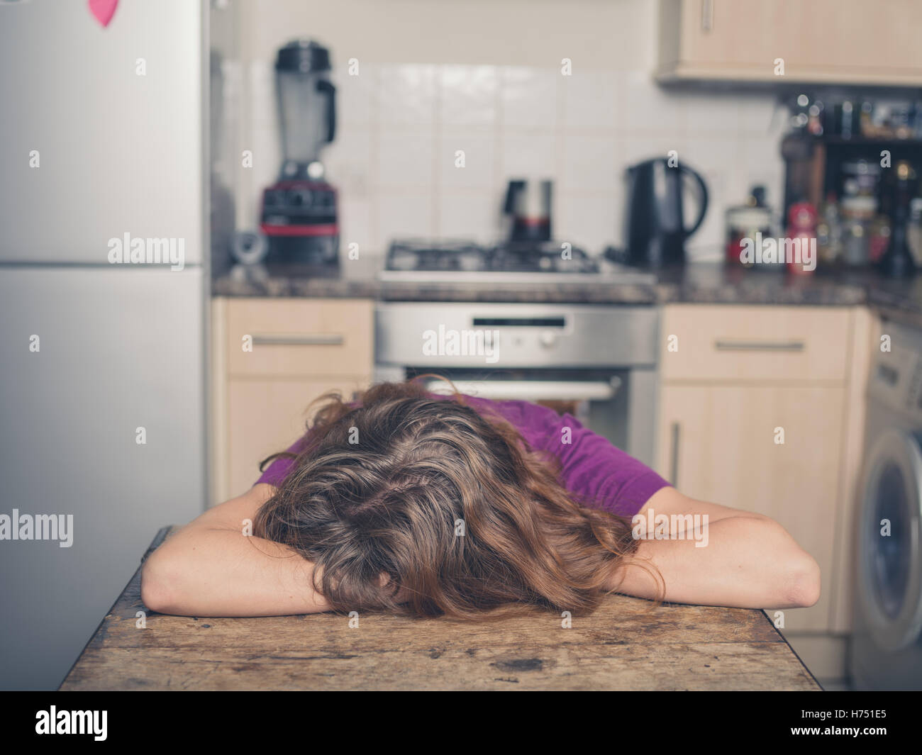 Une jeune femme se repose sa tête sur une table dans une cuisine Banque D'Images