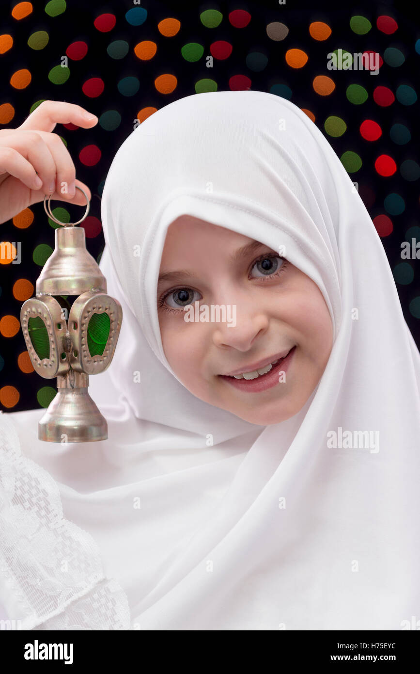 Jeune fille en blanc Hijab Holding Ramadan lanterne sur Nuit Lumières Fond flou artistique Banque D'Images