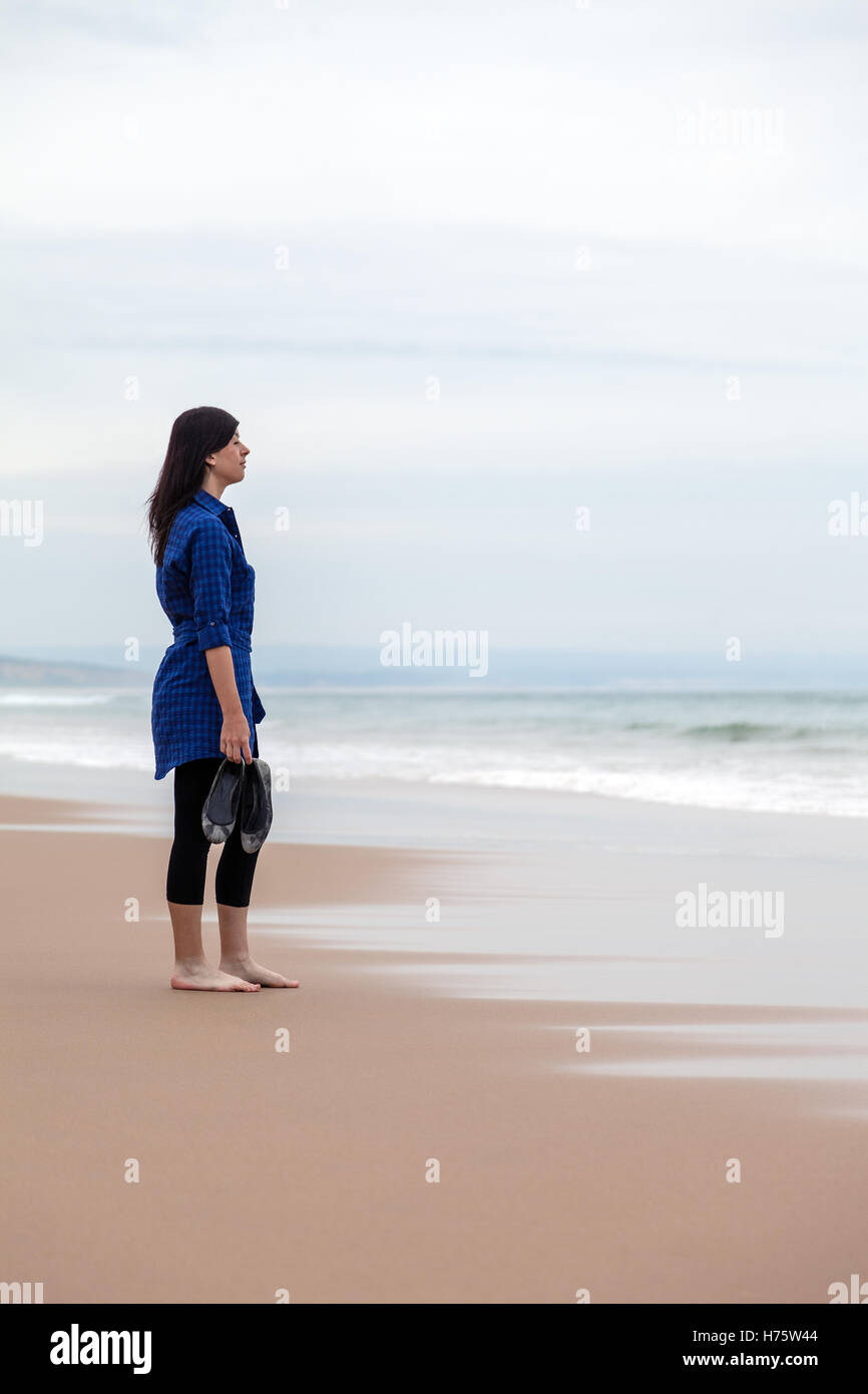 Seul et déprimé femme regardant la mer dans une plage déserte sur une journée d'automne. Banque D'Images