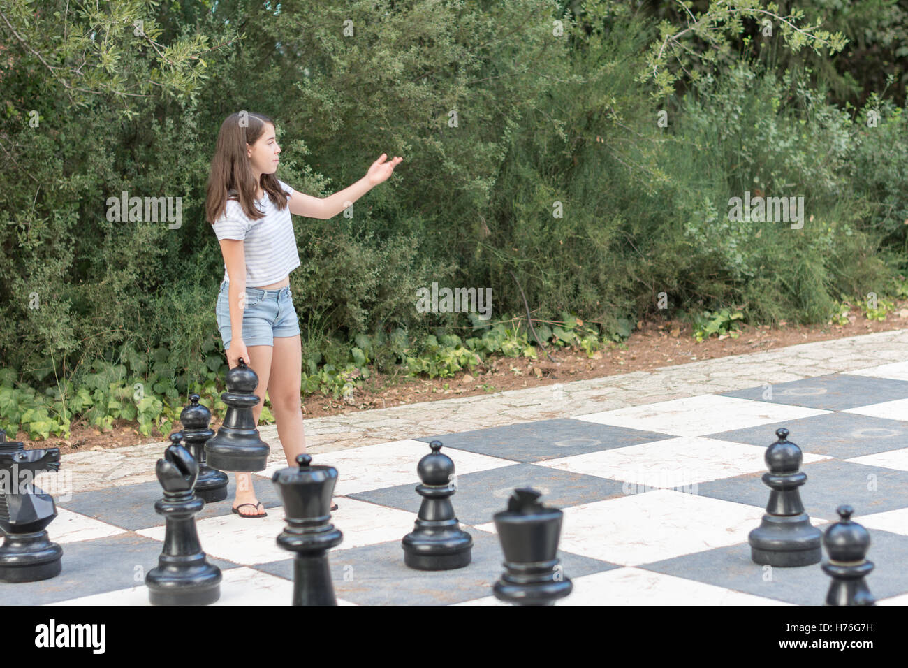 Teenage girl jouant un jeu d'échecs en plein air géant avec de gros morceaux dans un parc extérieur vert Banque D'Images