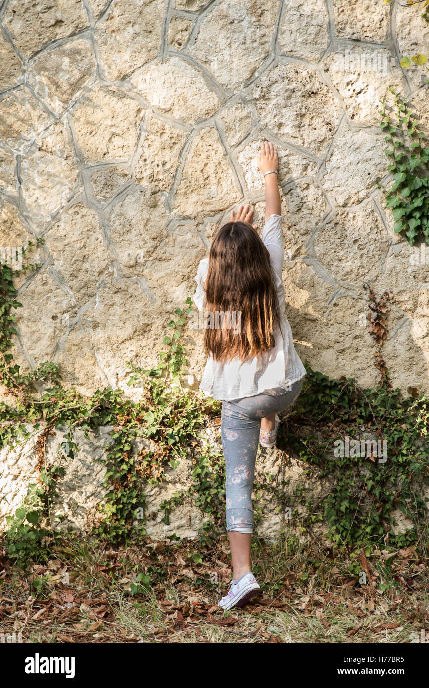 Girl climbing un mur dans le jardin Banque D'Images