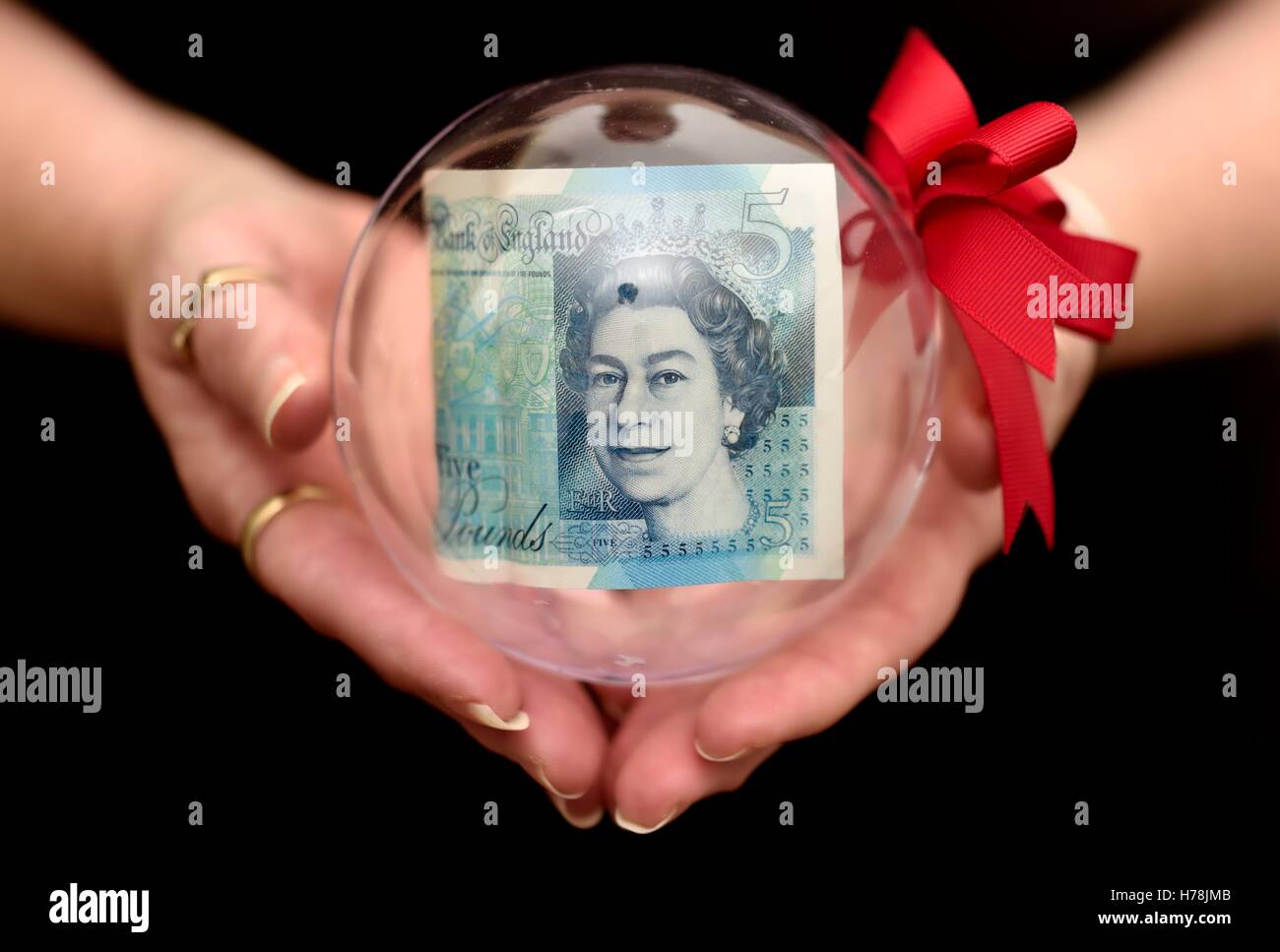Une note de cinq livres dans une boule de Noël en forme de coupe dans une main de femme. Banque D'Images