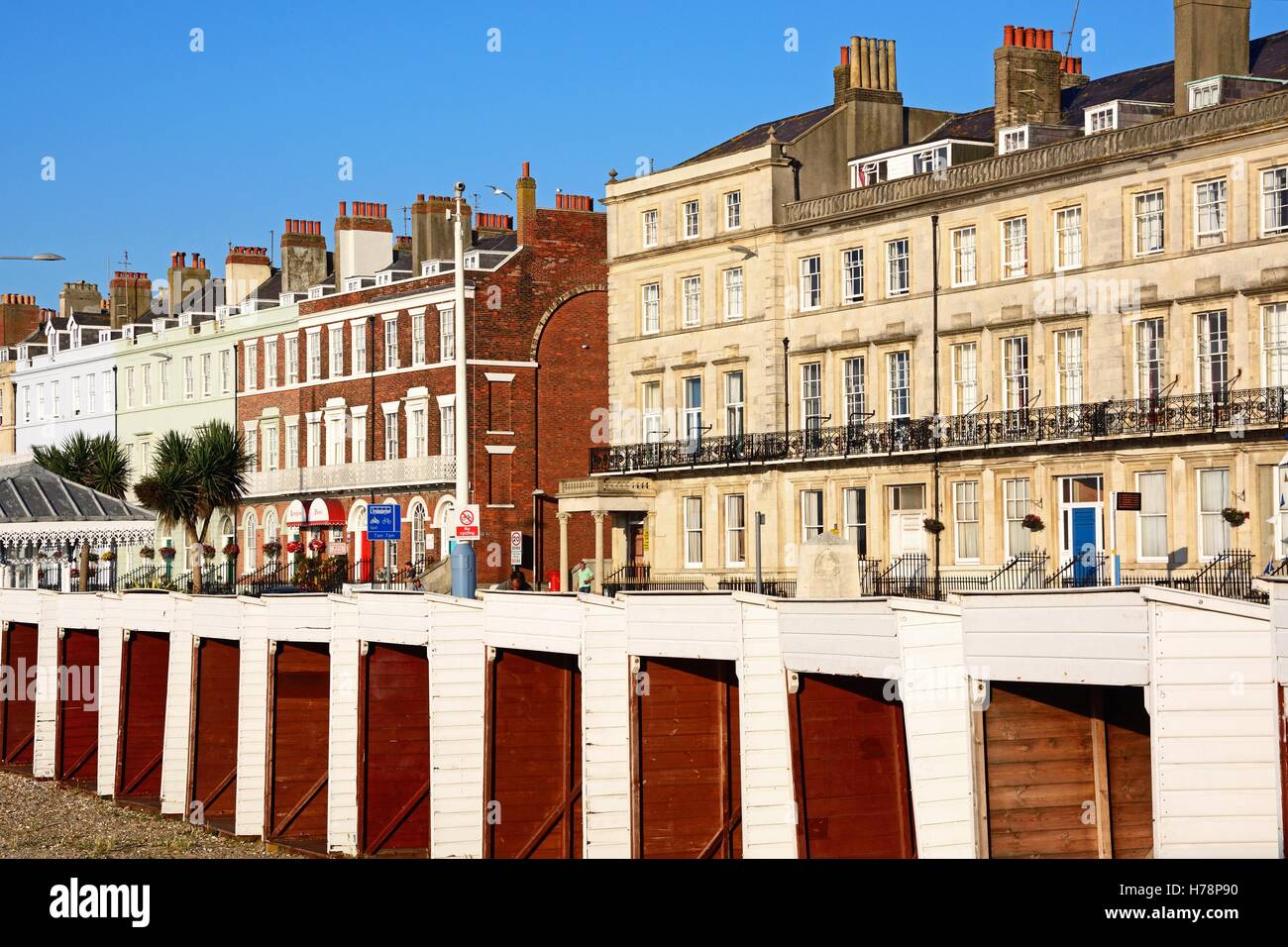 Rangée de maisons le long de la promenade de l'esplanade en bois avec des cabines de plage à l'avant-plan, Weymouth, Dorset, Angleterre, Royaume-Uni. Banque D'Images