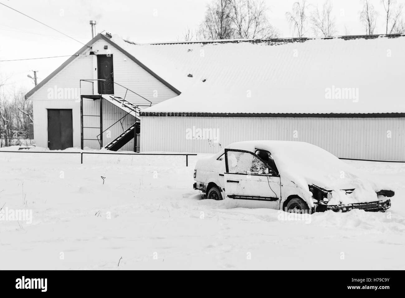 Voiture abandonnée dans la neige près de maisons abandonnées en noir et blanc Banque D'Images