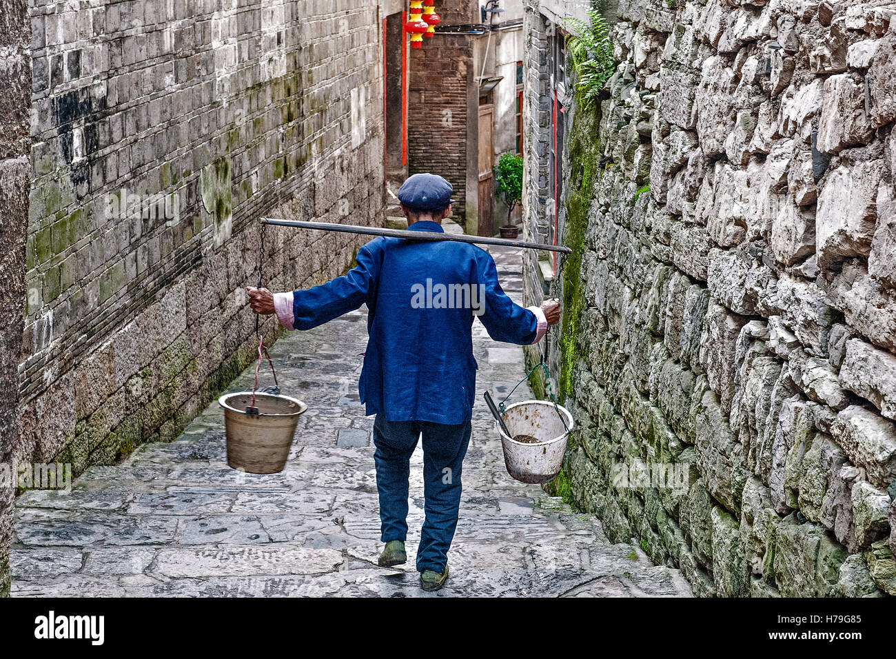 Un vieil homme portant un balancier à travers une rue de l'ancien village en pierre Zhenyuan, Guizhou, Chine Banque D'Images