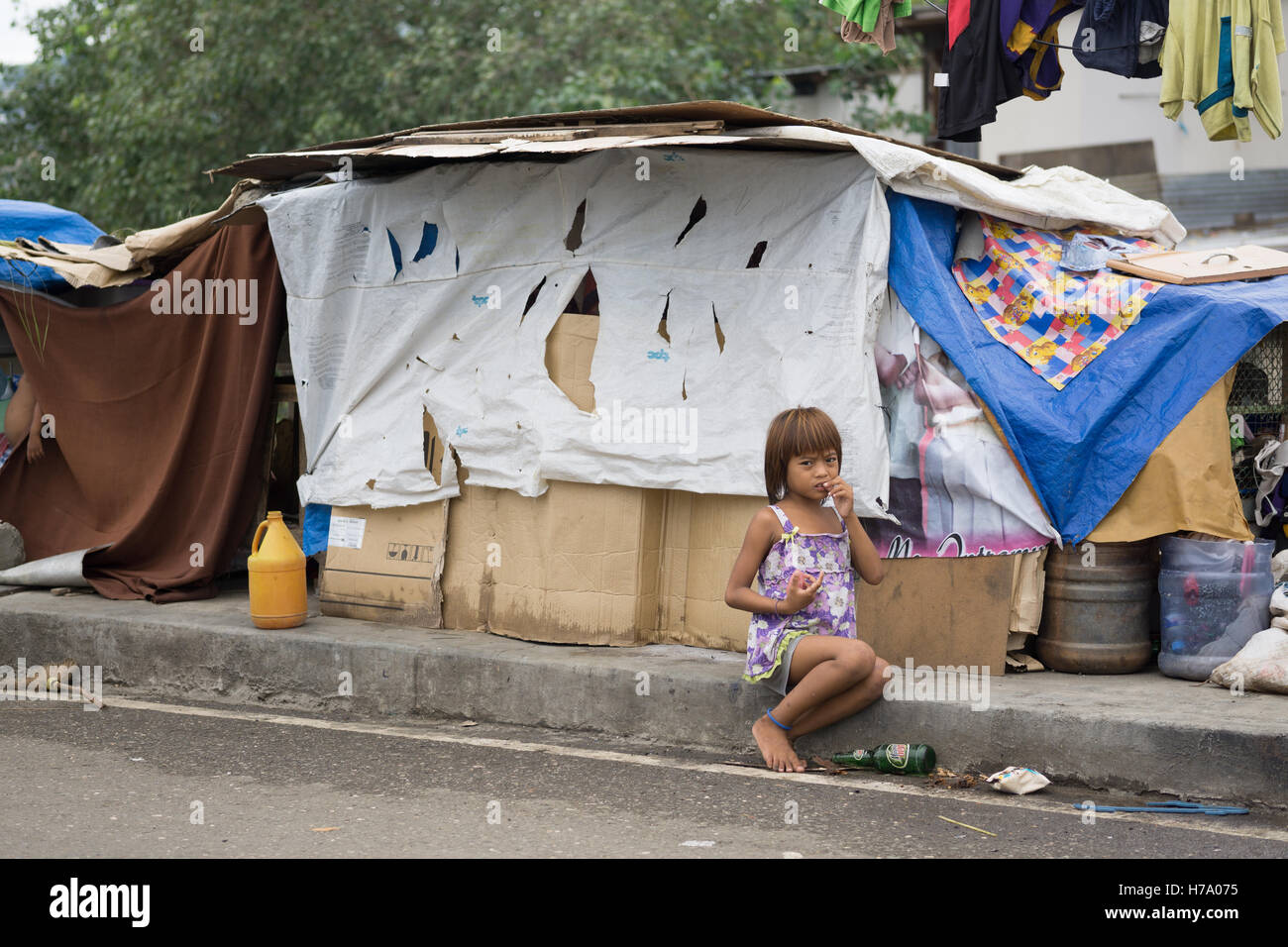 Enfant philippin assis sur la chaussée à l'extérieur de sa maison en carton, Cebu City, Philippines. Banque D'Images