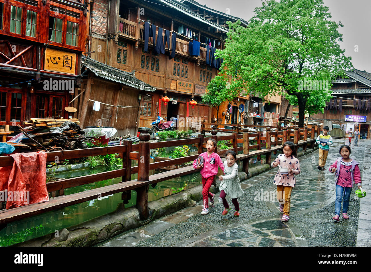 Baby-filles exécutant le long d'une rue près de la rivière à côté d'une ligne des hautes maisons bois de Zhaoxing, dans la province de Guizhou, Chine Banque D'Images