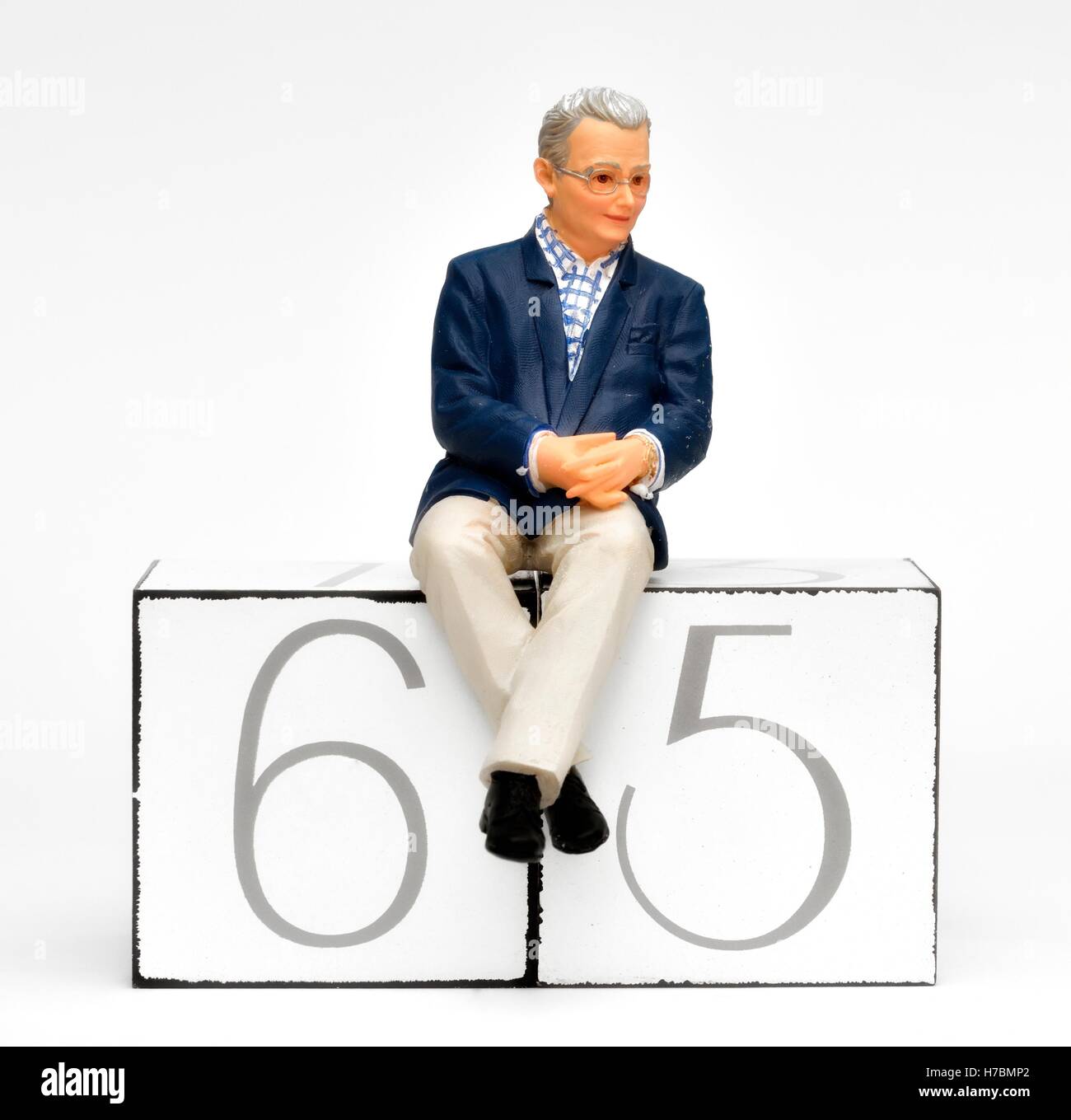 Une figurine homme retraité assis sur le nombre 65 concept de la retraite. Banque D'Images