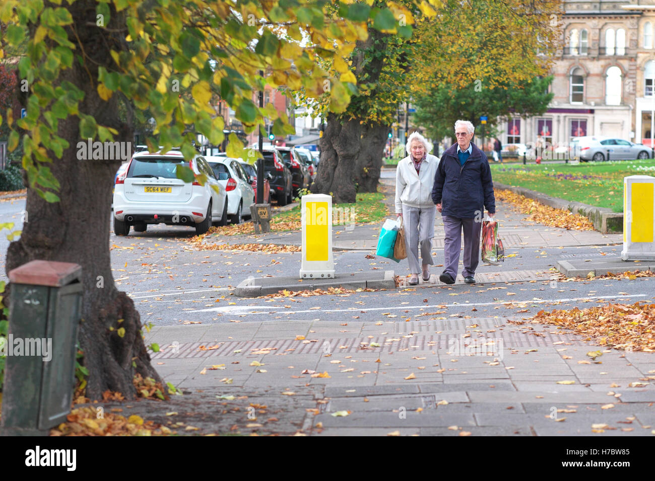 Harrogate North Yorkshire UK couple de retraités âgés man and woman carrying shopping bags par les automnes leaves Banque D'Images