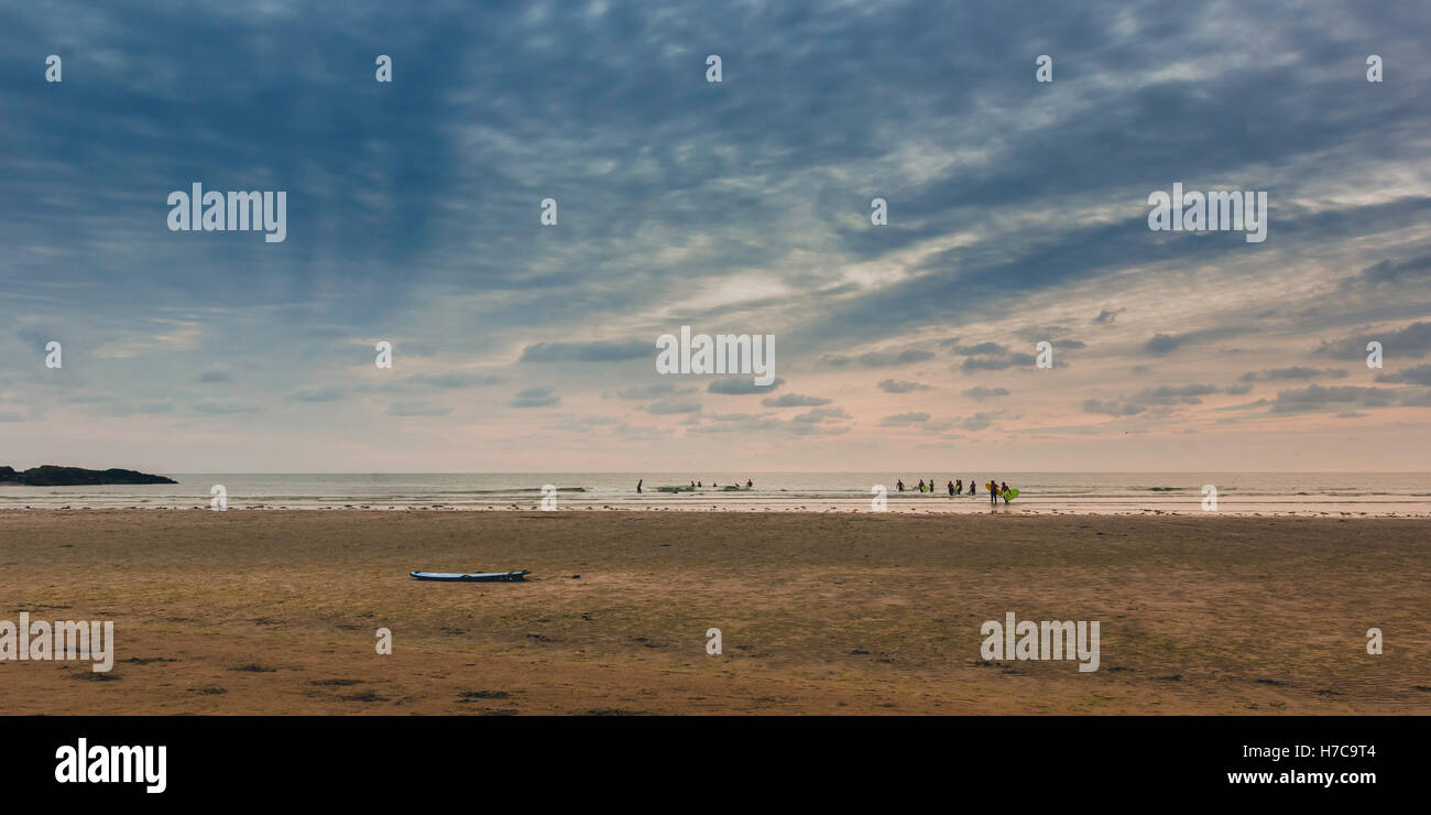 Le dirigeant d'une planche repose sur la plage sable comme les surfeurs sortent en mer dans le dernier de la lumière du jour. Clonakilty, Irlande, 2016 Banque D'Images