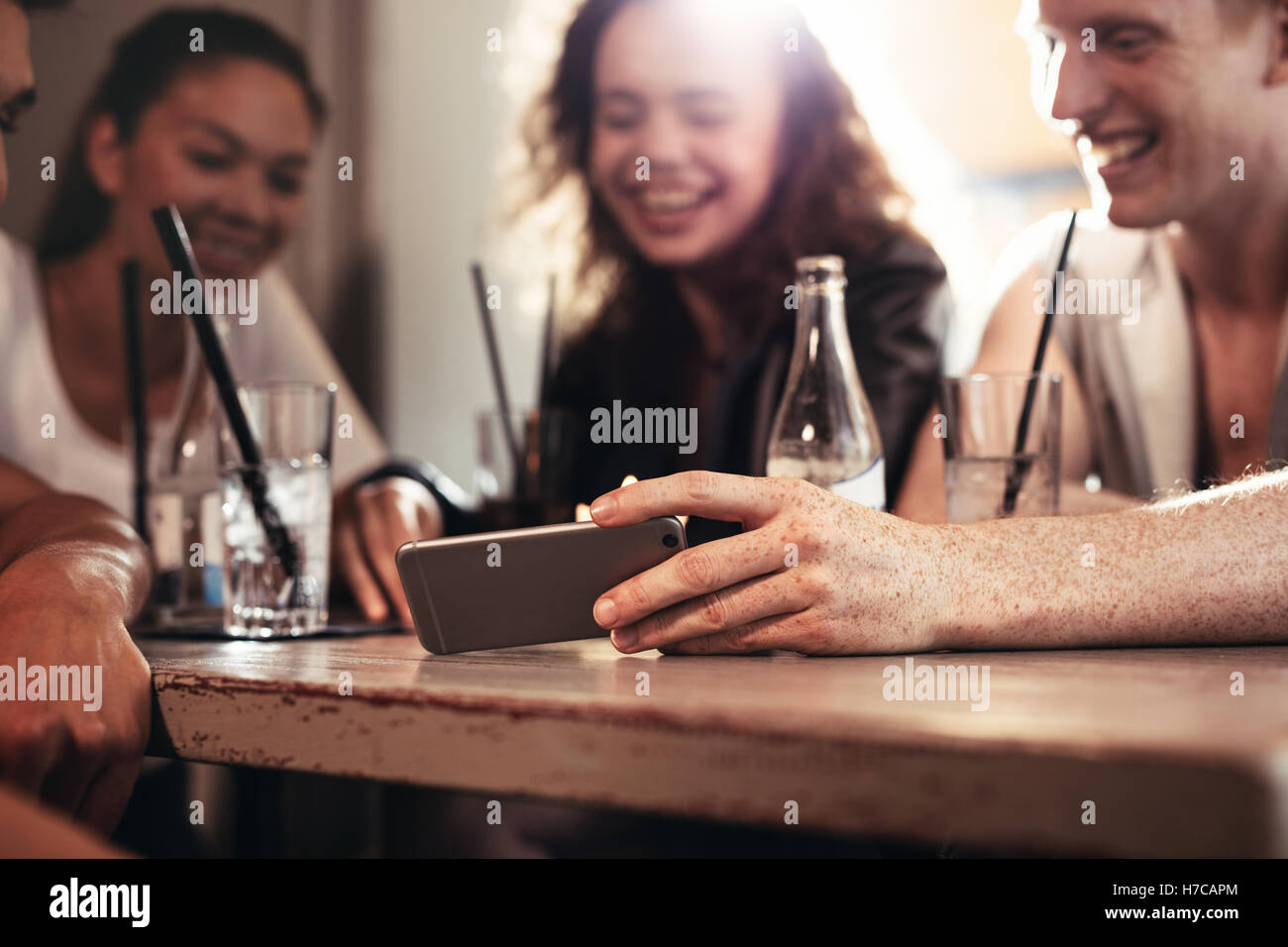 Groupe d'amis assis dans un bar et regarder une vidéo amusante sur téléphone mobile, l'accent sur téléphone mobile dans l'homme de main. Banque D'Images