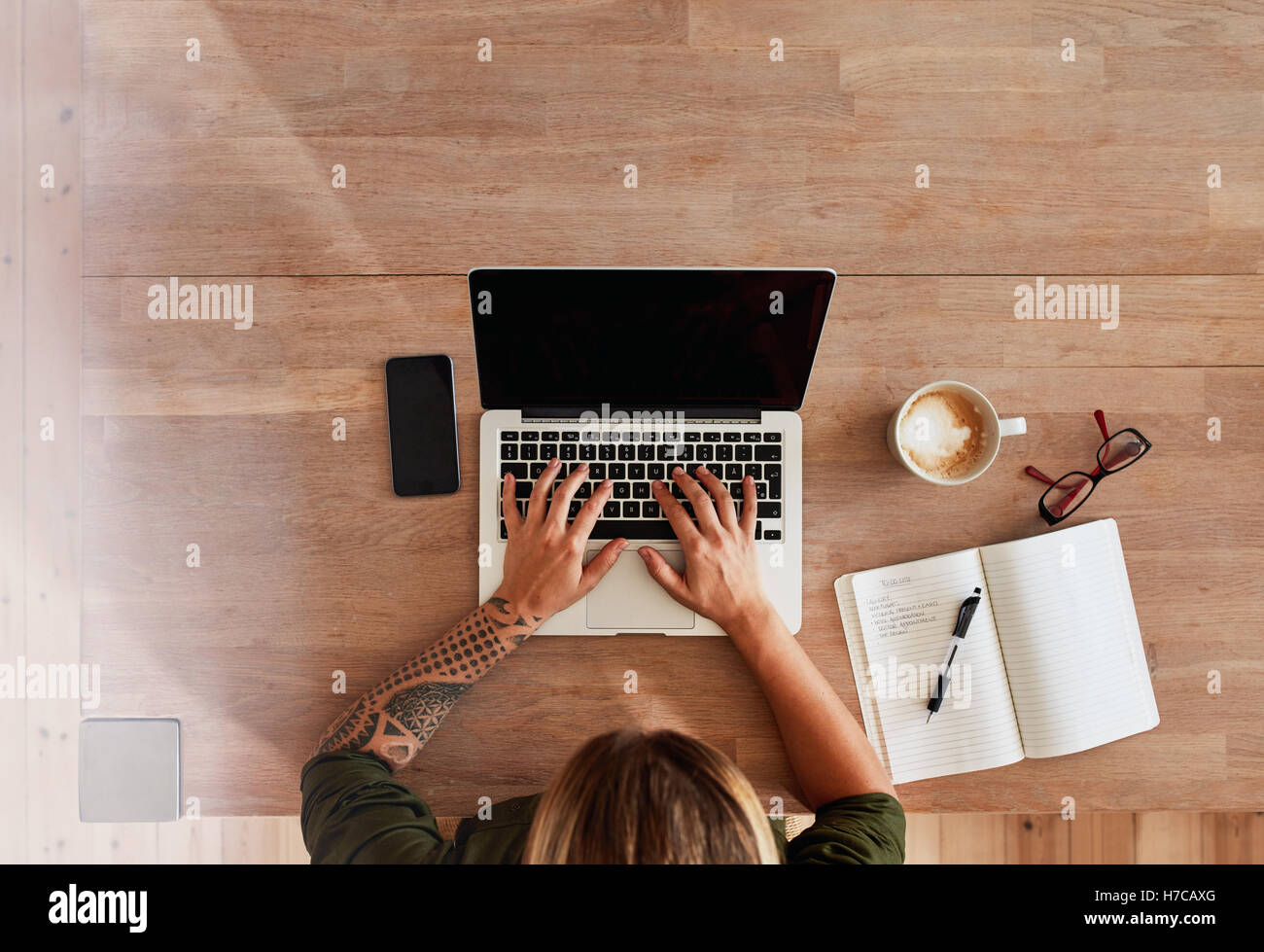 Top View of woman typing on laptop mains. Lieu de travail avec ordinateur portable, smartphone, journal et tasse à café. Femme travaillant à la maison. Banque D'Images