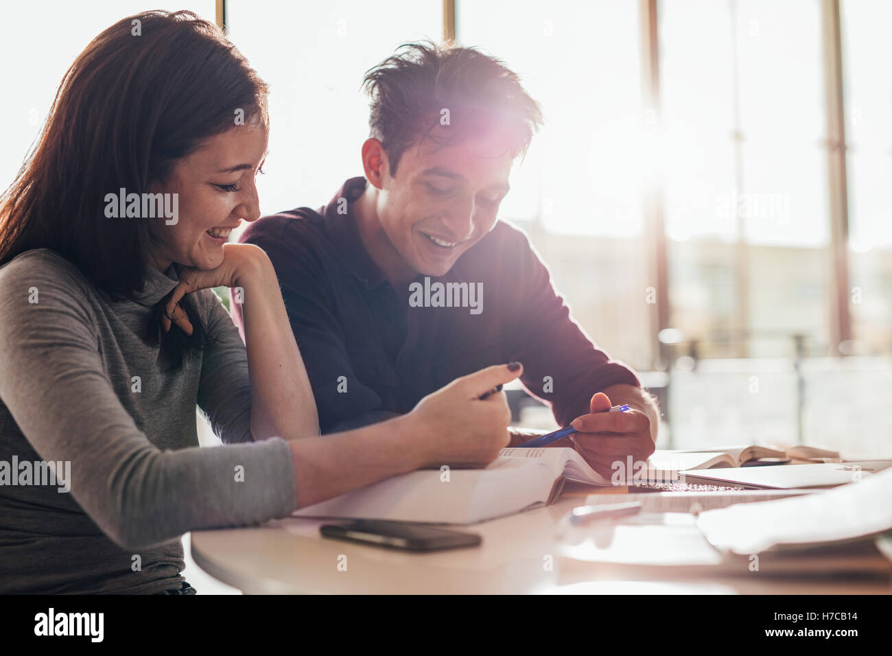Heureux jeunes étudiants hommes et femmes lisant un livre ensemble en classe. étudiants universitaires étudiant ensemble en bibliothèque. Banque D'Images