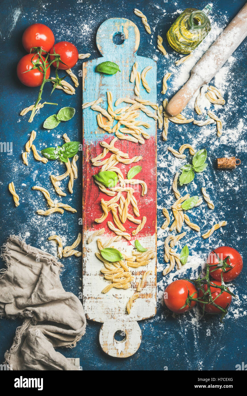 Ingrédients pour cuisiner un dîner italien. Pâtes fraîches casarecce, cherry-tomates, feuilles de basilic et de bouteille d'huile d'olive on colorful Banque D'Images