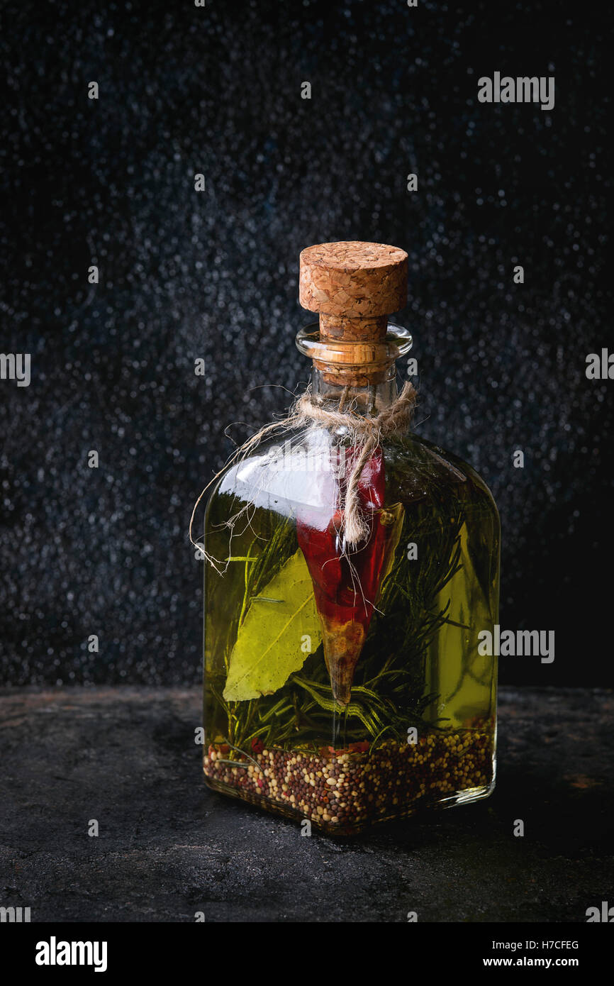 Bouteille de verre d'huile d'olive épicée au romarin, Red Hot Chili Peppers et le laurier sur fond texturé noir permanent. Medit Banque D'Images