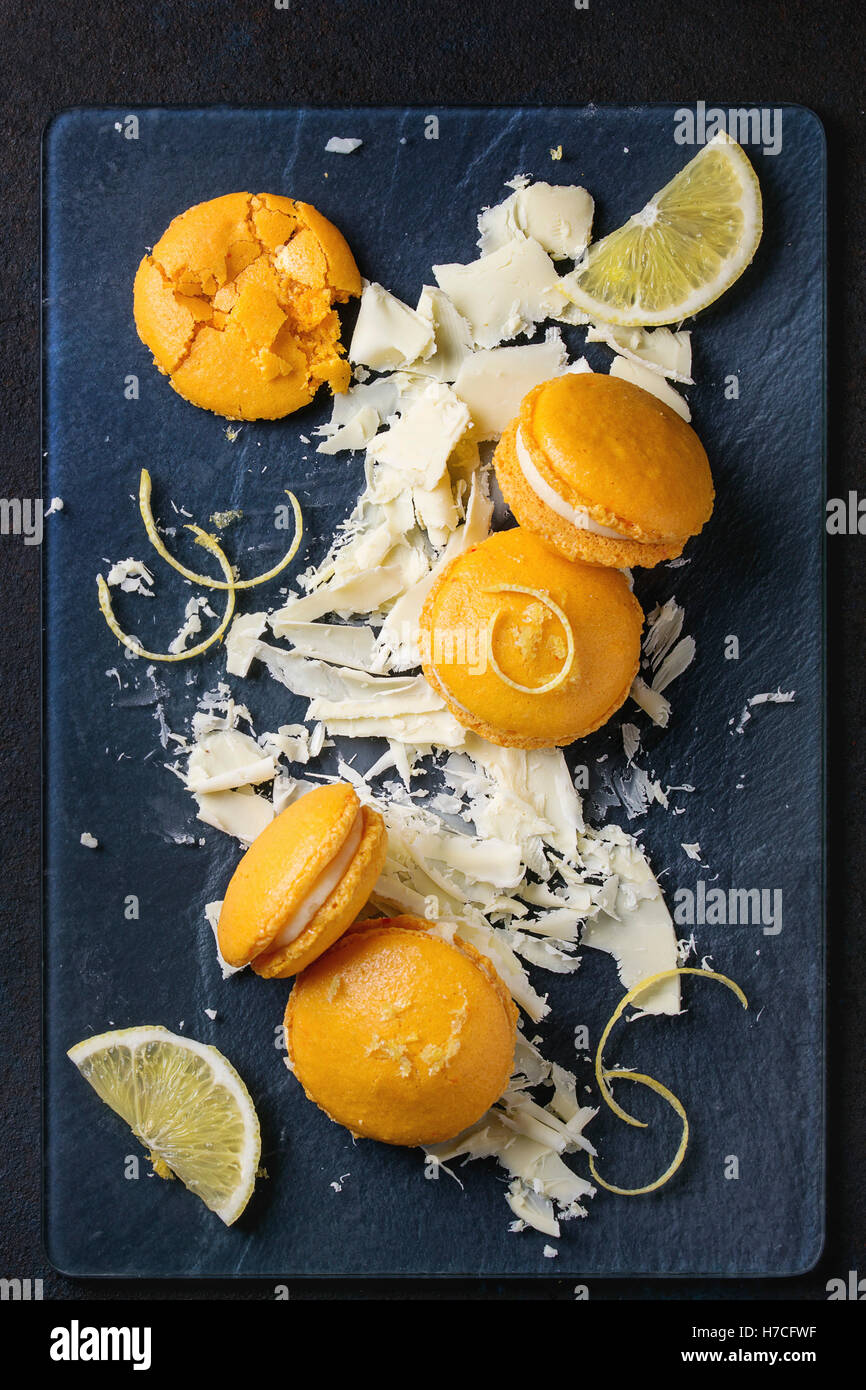 Ensemble et broken orange citron macarons fait maison avec des morceaux de chocolat blanc et le sucre et le zeste de citron sur le verre foncé plus de conseil Banque D'Images