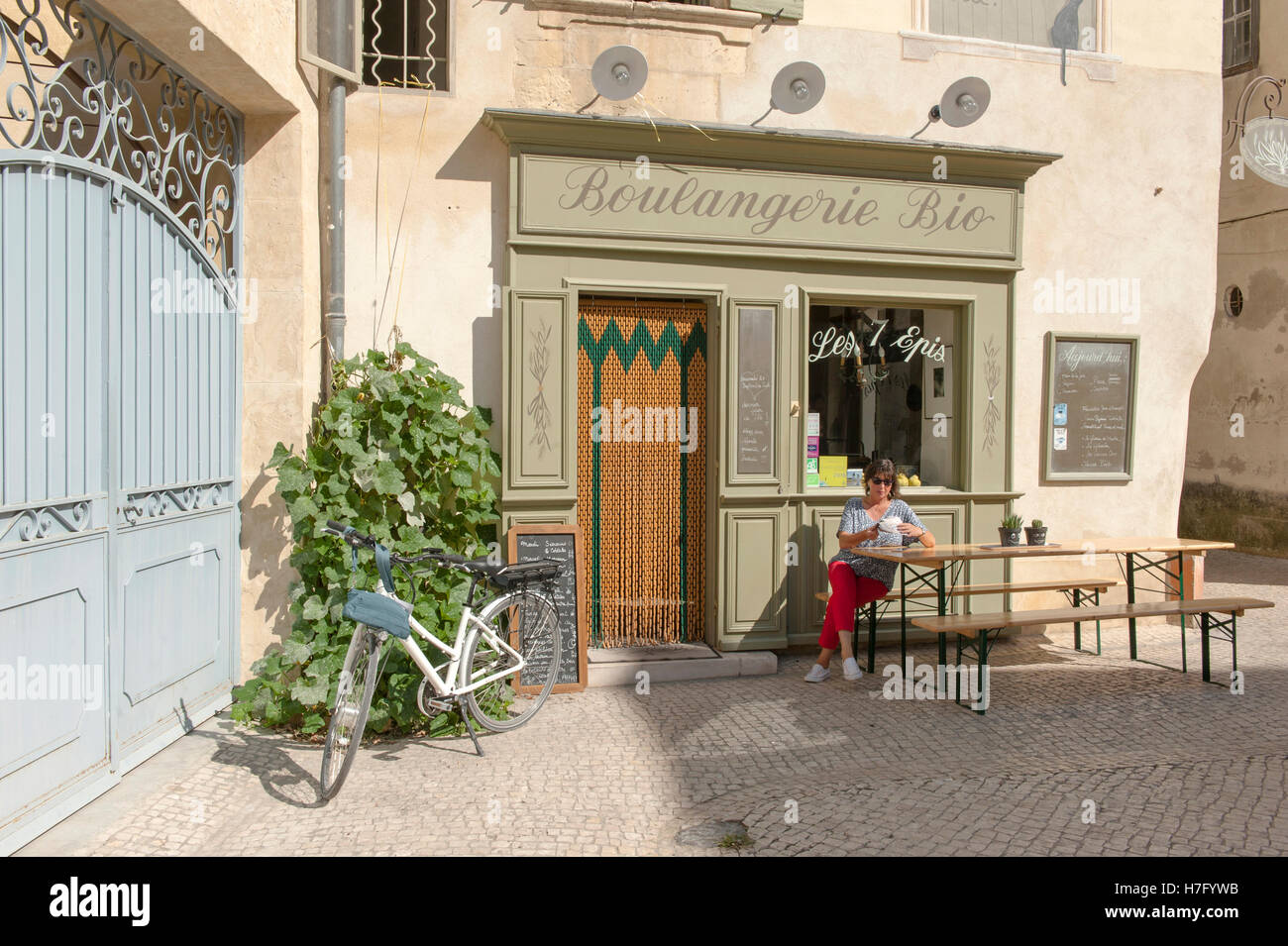 Cycliste féminine Claudia (Albrecht) assis sur un banc en face d'une boulangerie éco à Tarascon, Provence, France Banque D'Images