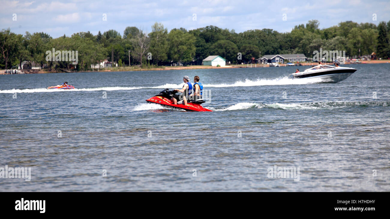 Bord de l'activité avec bateau de vitesse en tirant les enfants sur un tube d'eau alors que des adolescents passent sur un jet ski. Clitherall Minnesota MN USA Banque D'Images