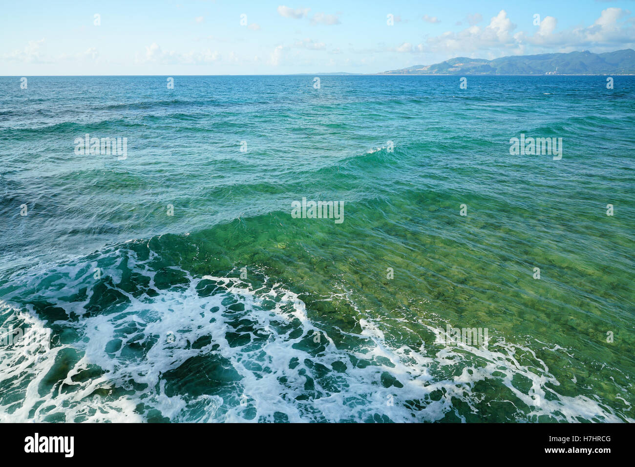 Vague et de la mousse sur le bleu de la mer avec l'arrière-plan de la partie continentale. Banque D'Images