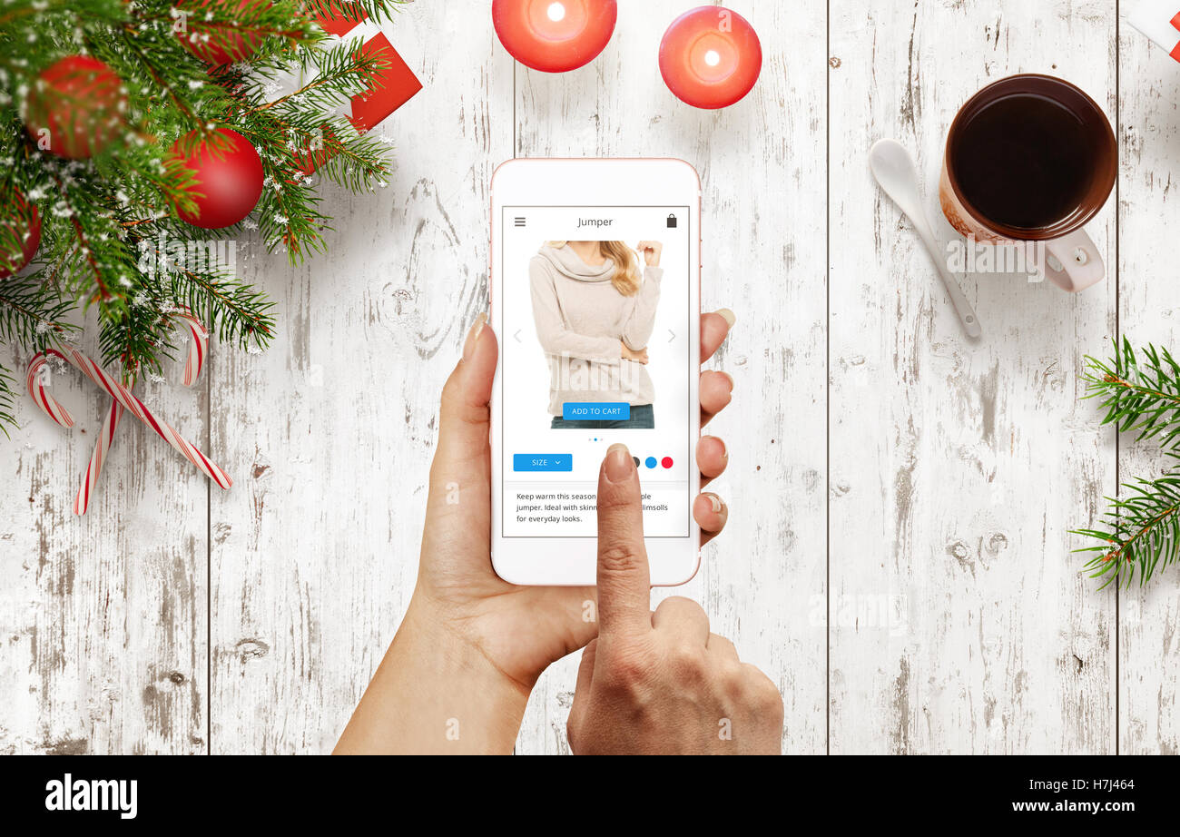 Femme acheter sauteur avec smart phone pendant la période de Noël. Table avec arbre de Noël, décorations, cadeau, bougie, thé Banque D'Images